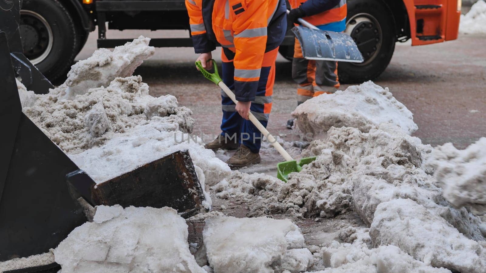 Tractor shovel loading snow and ice into truck during winter road cleaning.