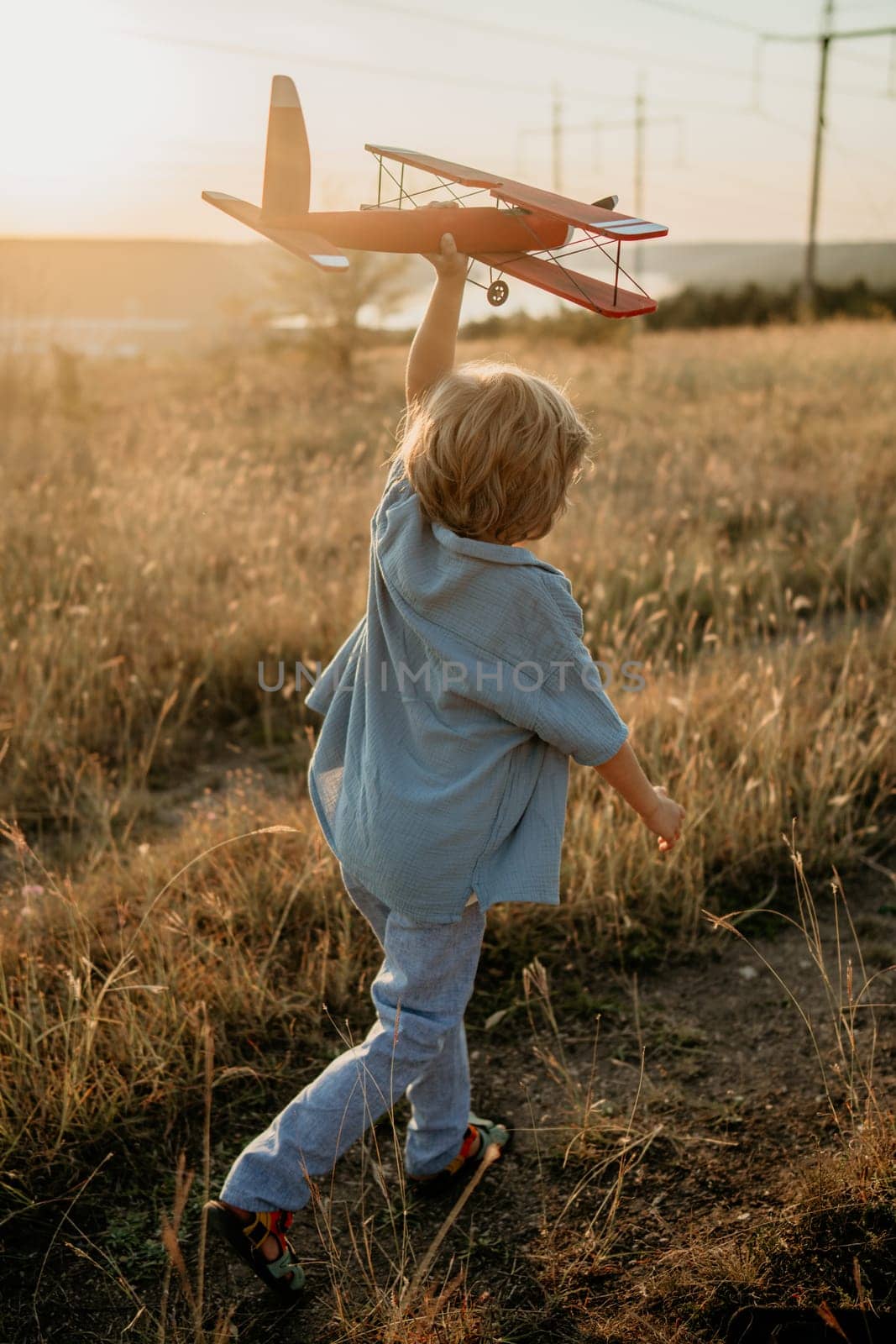 Unrecognizable 5 years old child boy running with wooden vintage airplane. Kid dreaming to be pilot. Imagination freedom, travel everywhere, active childhood. High quality