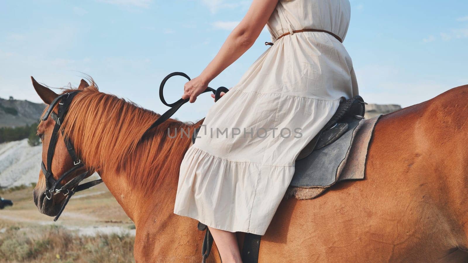 Woman wearing long white dress riding brown horse in the mountains of Crimea near the town of Belogorsk