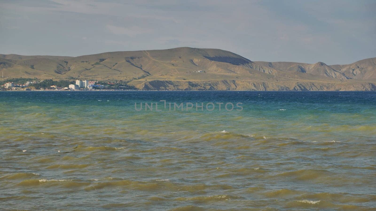 Windsurfing across blue waves near rocky crimean shoreline, bright sunlight highlighting water and distant coastal landscape