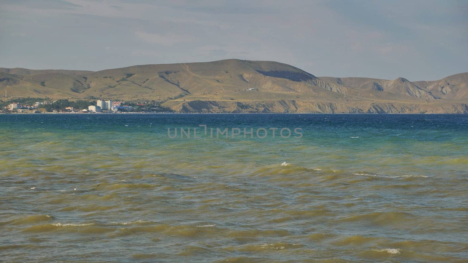 Small waves gently rolling in Koktebel bay, with mountains and buildings in the background