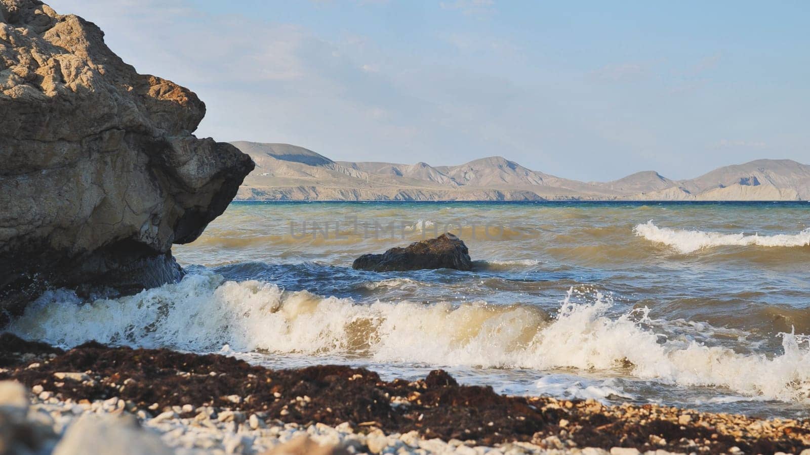 Seascape with waves crashing on Crimean beach with rocks and mountains in the distance