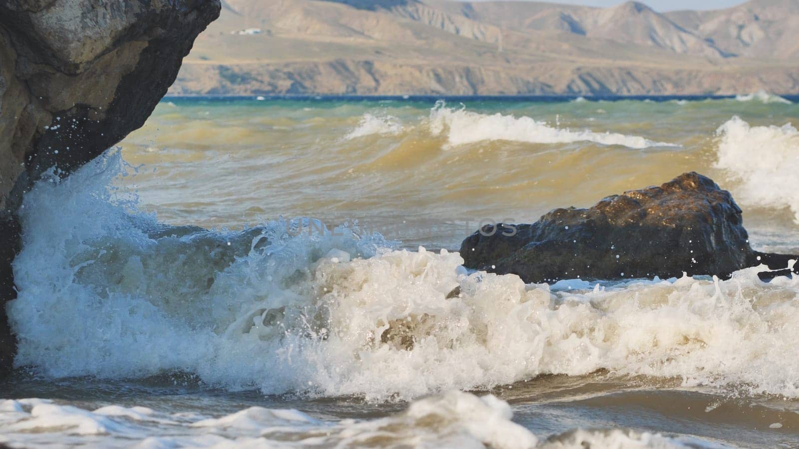 Waves crashing on rocks in Crimea, Black Sea with mountains in background