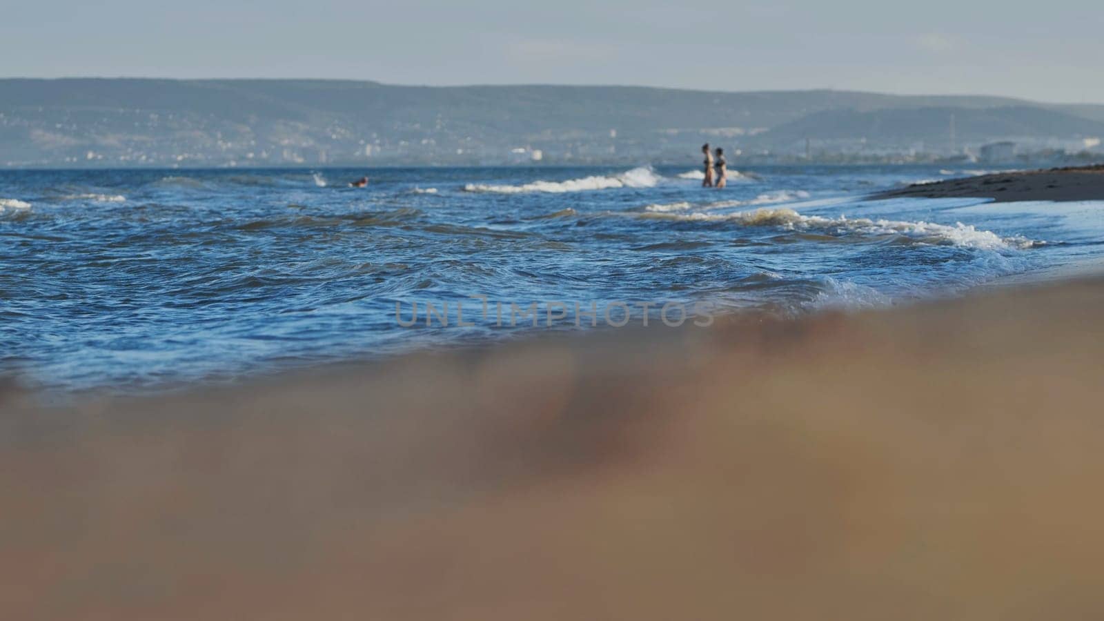 Sea waves washing sandy beach in Crimea with tourists enjoying summer vacation on a beautiful sunny day