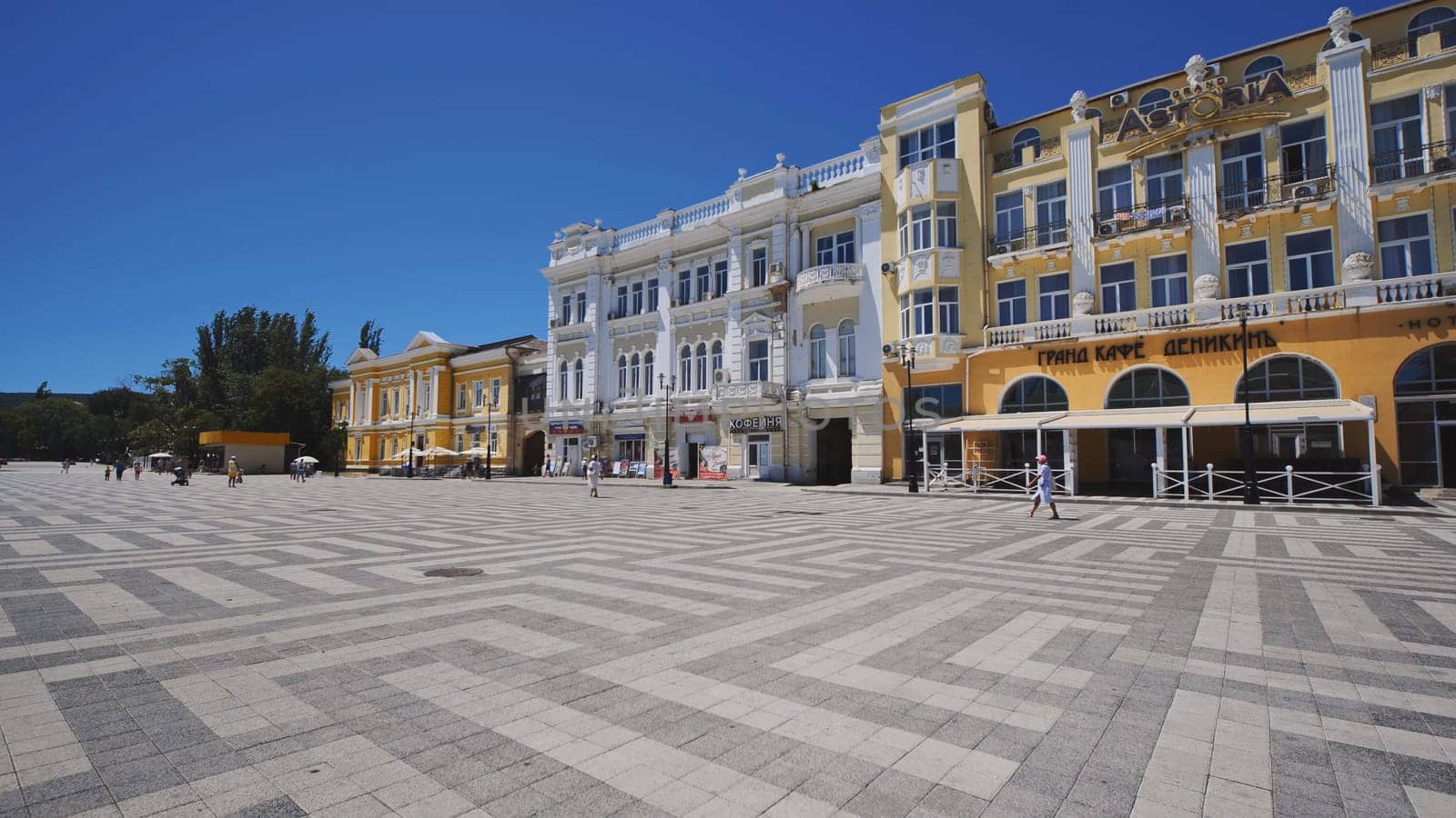 Tourists walking in Nakhimov Square with colorful buildings under blue sky in Sevastopol, Crimean peninsula