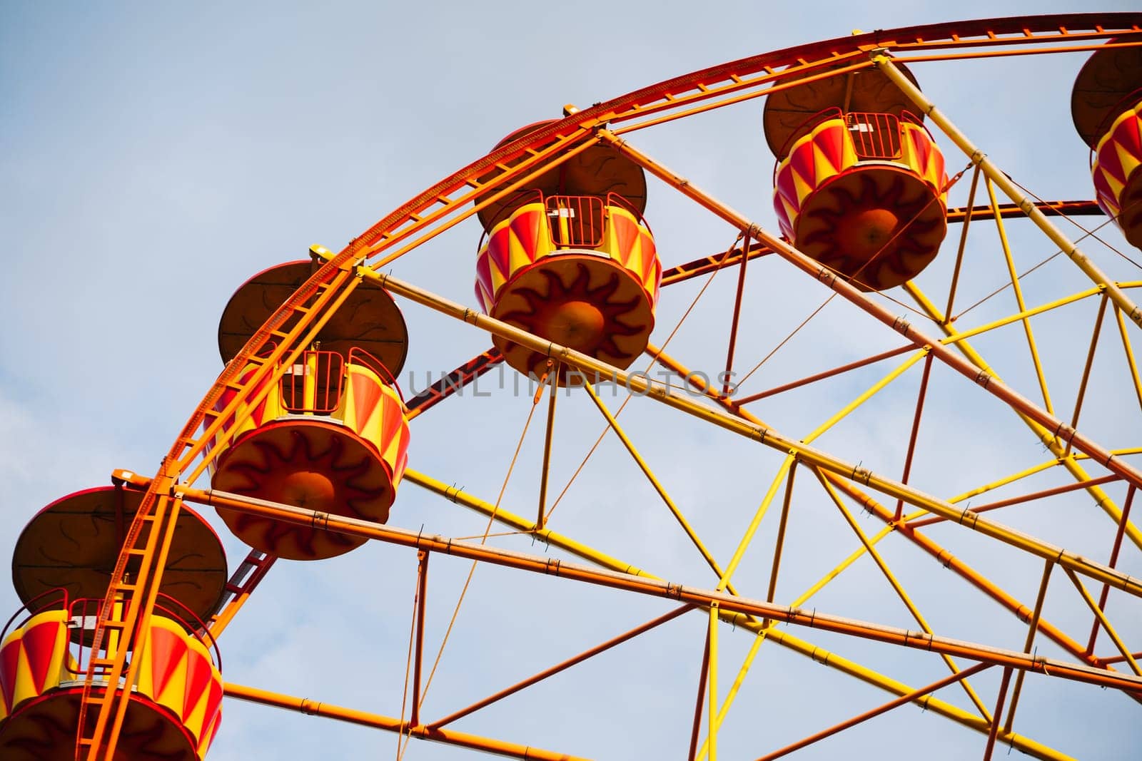 Ferris wheel with yellow and red cabins rotating in amusement park under blue sky in Crimea