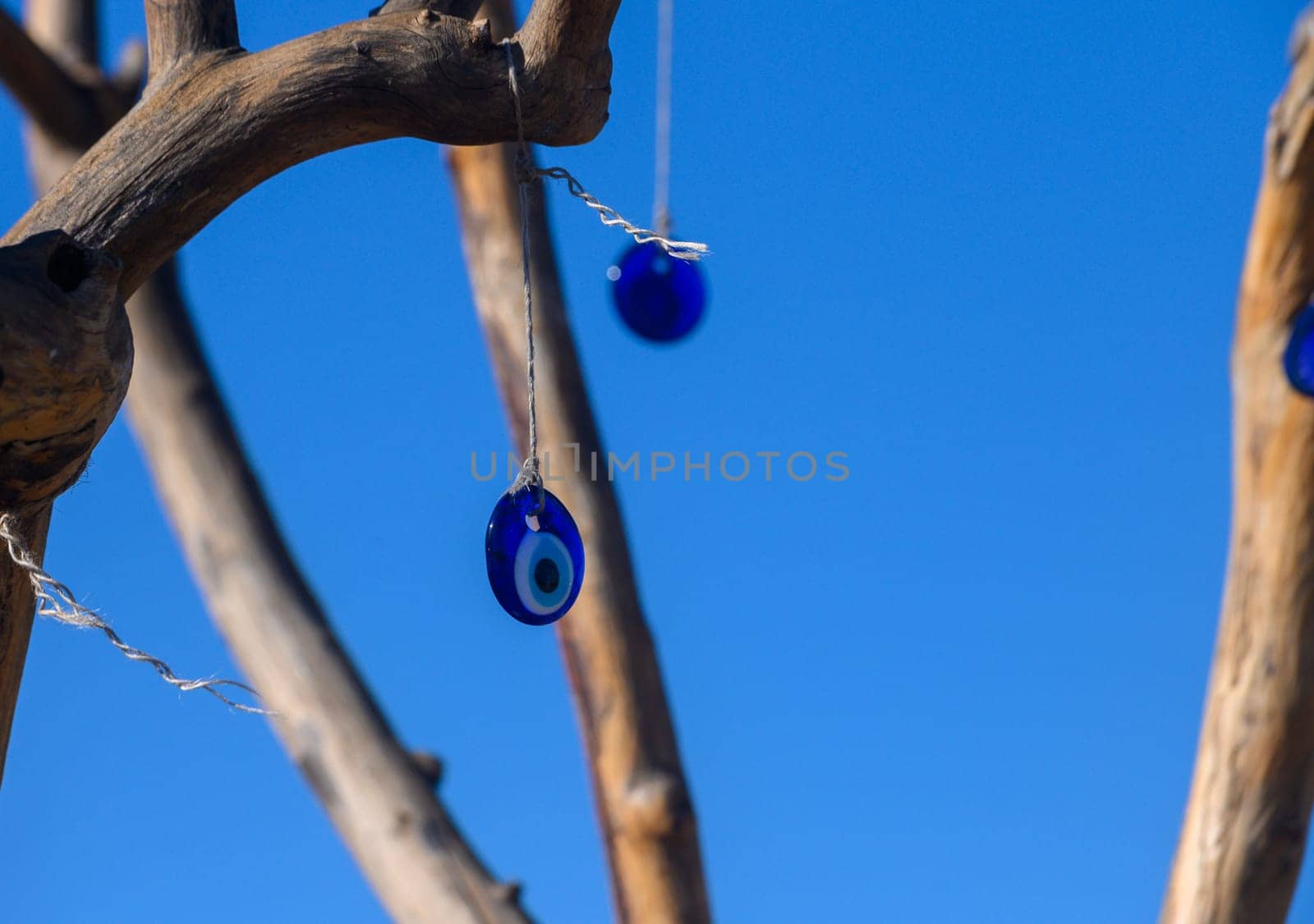 Colorful blue amulets, traditionally believed to protect from negative energy, dangle gracefully from a rustic tree against a backdrop of clear blue skies. Art and nature unite beautifully.