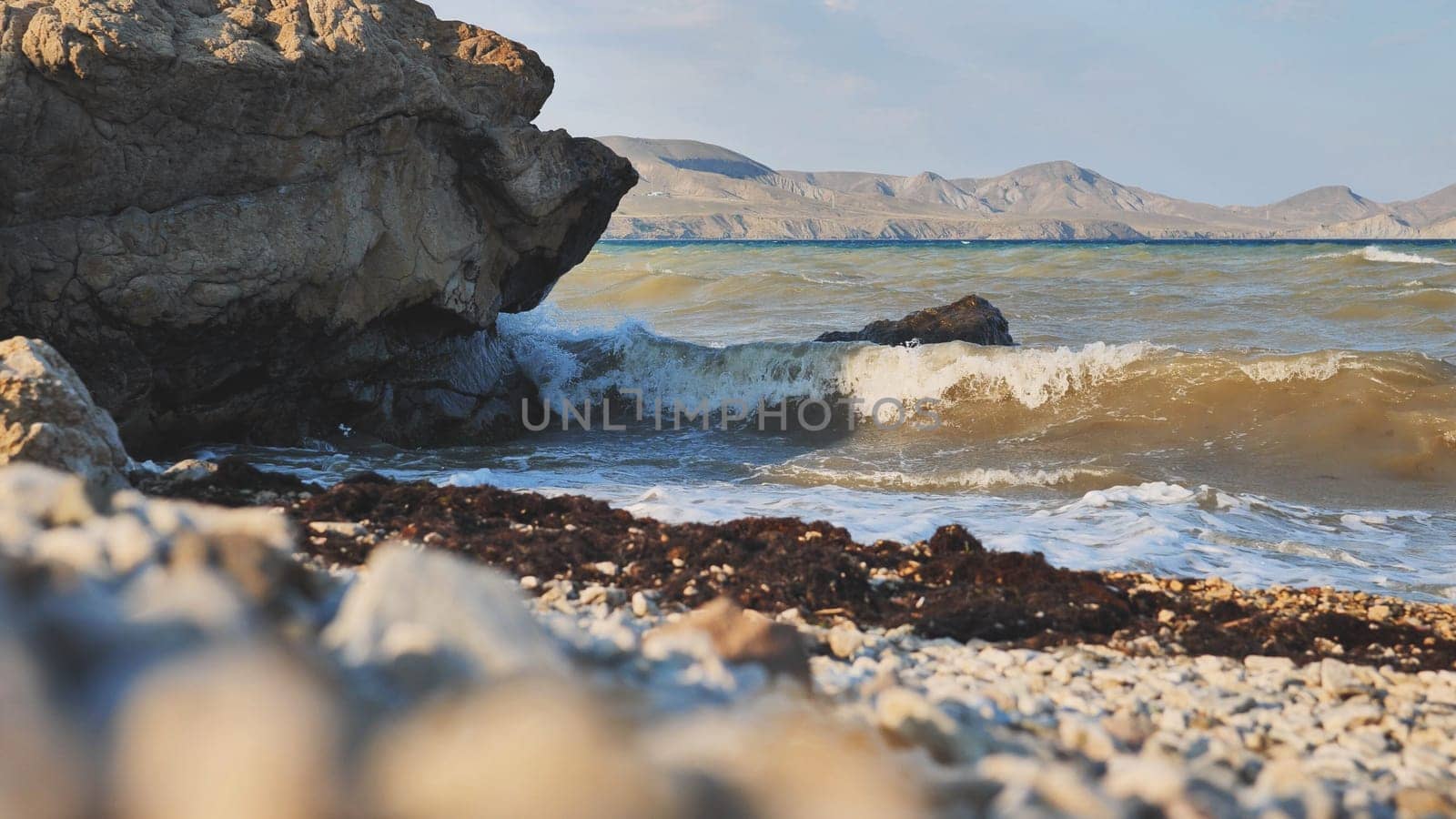Scenic view of waves crashing on a rocky beach in Crimea, with mountains visible in the distance during a beautiful sunset