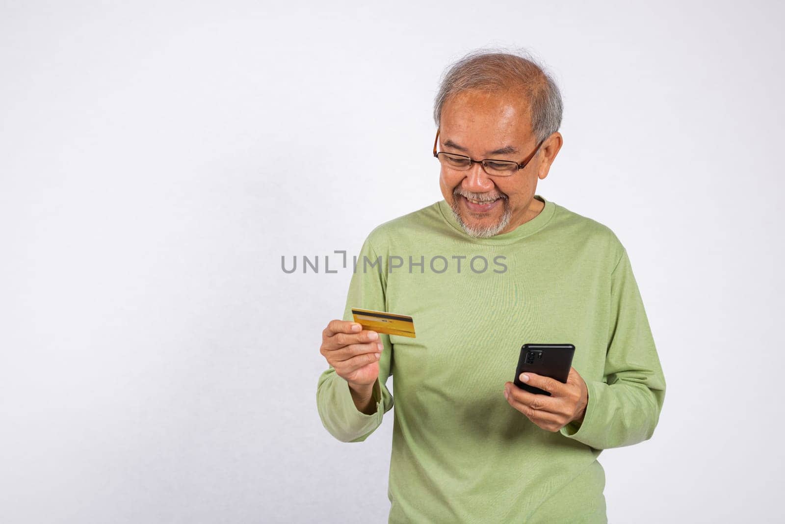 Portrait Asian smiling old man is holding a credit card and a cell phone. He is likely checking his bank account balance or making a purchase studio shot isolated on white background
