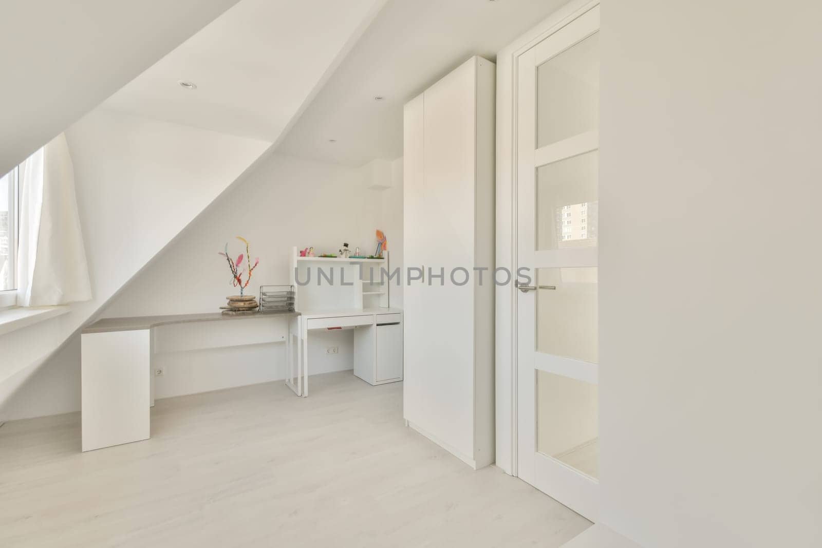 a bedroom with white walls and wooden flooring, an open door to the left is a small desk on the right side