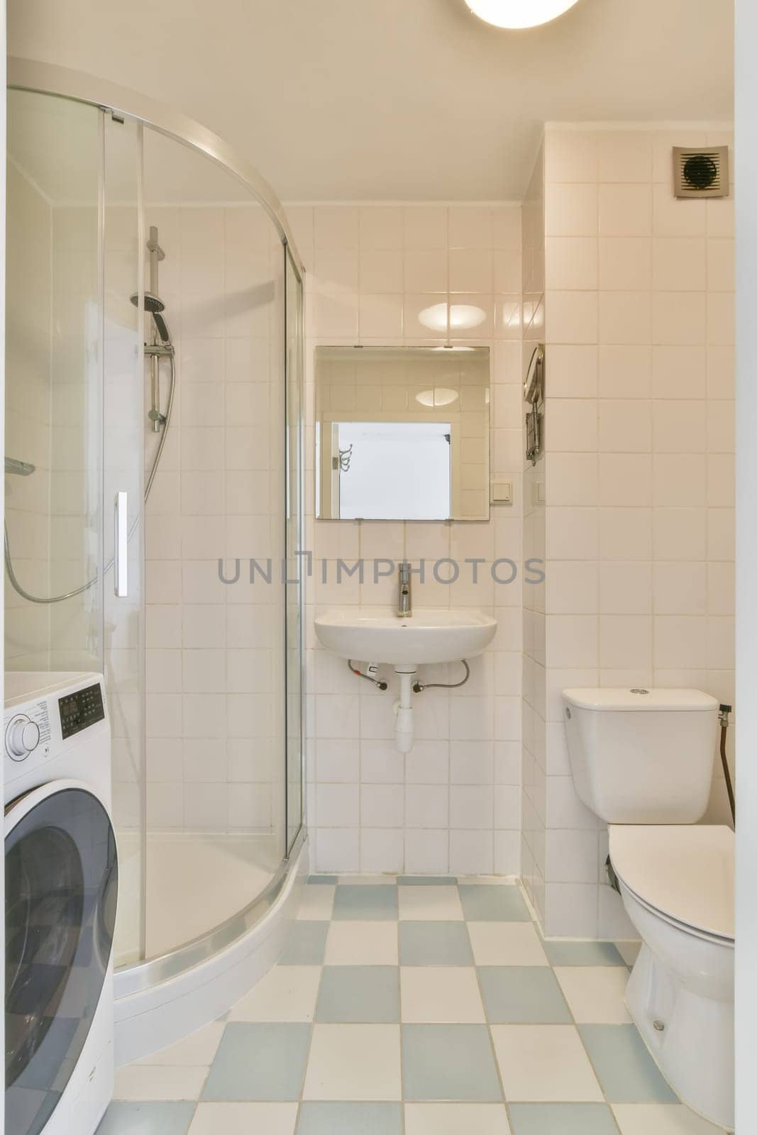 a white and blue tiled bathroom with a washer, toilet, and washing machine in the photo is taken