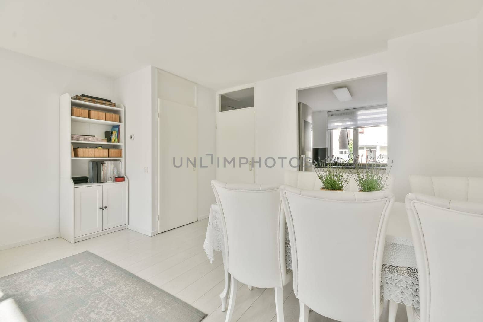 a dining room with white furniture and an open door that leads to the living area there is a large window