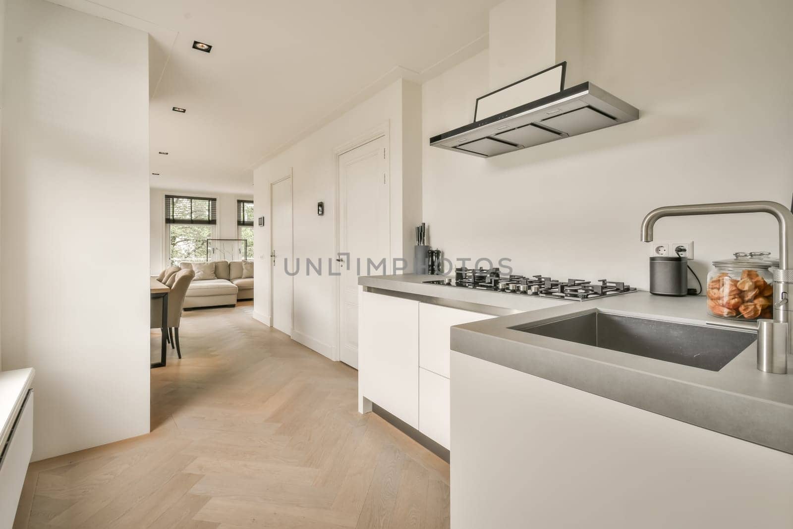 a modern kitchen with wood flooring and white cabinetry in the room is also furnished by an open - plan living area