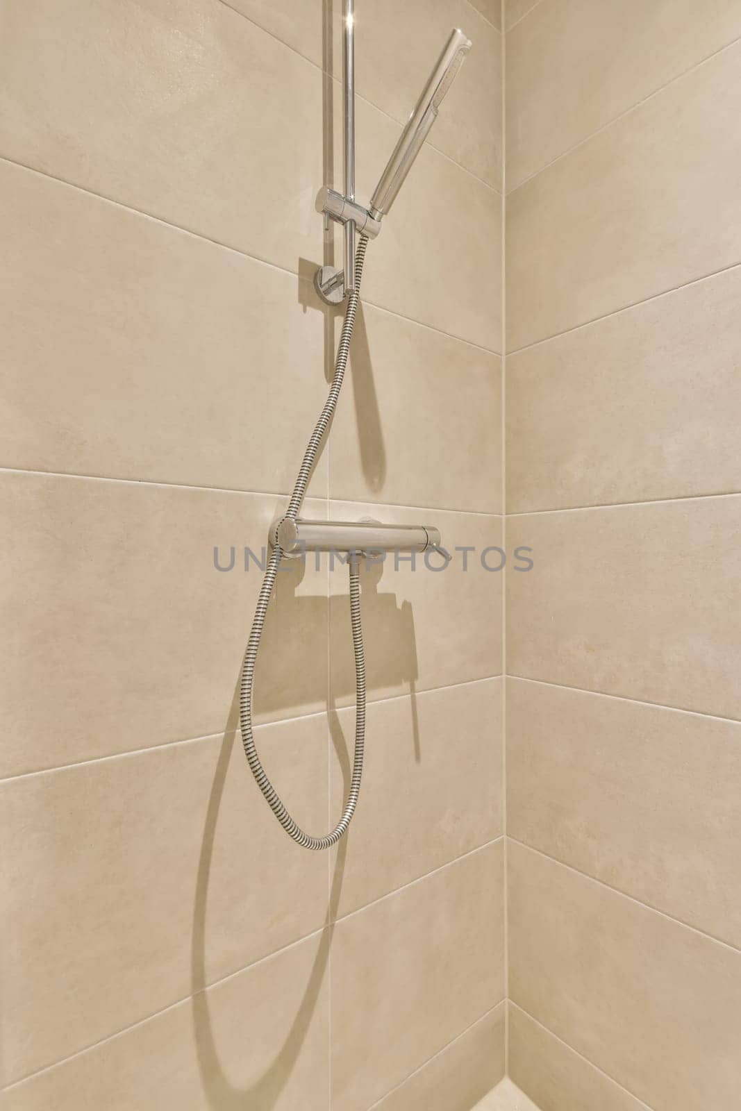 a shower with a hand held shower head and handset on the wall, in a white tiled bathroom background