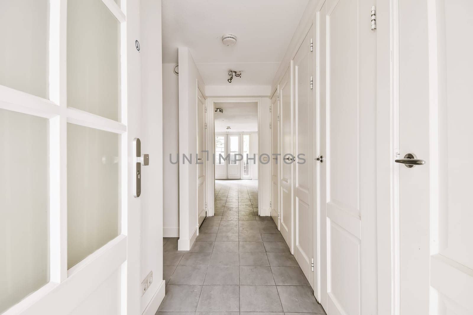 a long hallway with tile flooring and white trim on the walls, leading to an open door that leads to another room