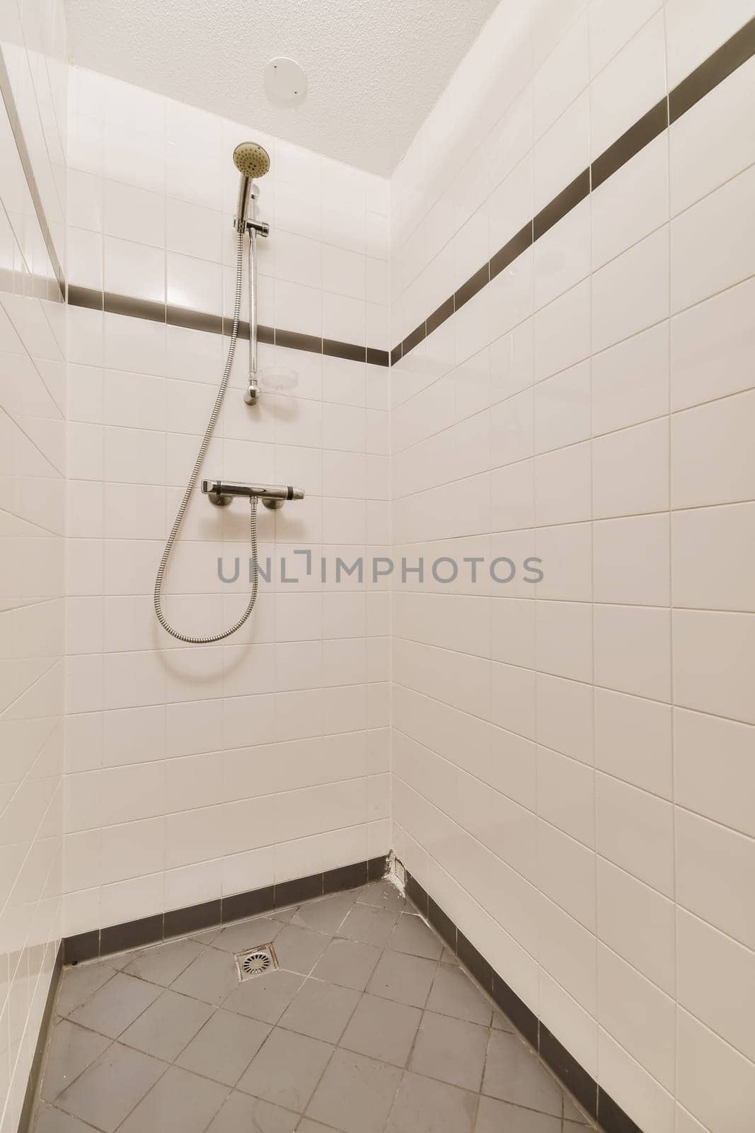 a bathroom with tile flooring and white tiles on the walls, including a shower head mounted to the wall