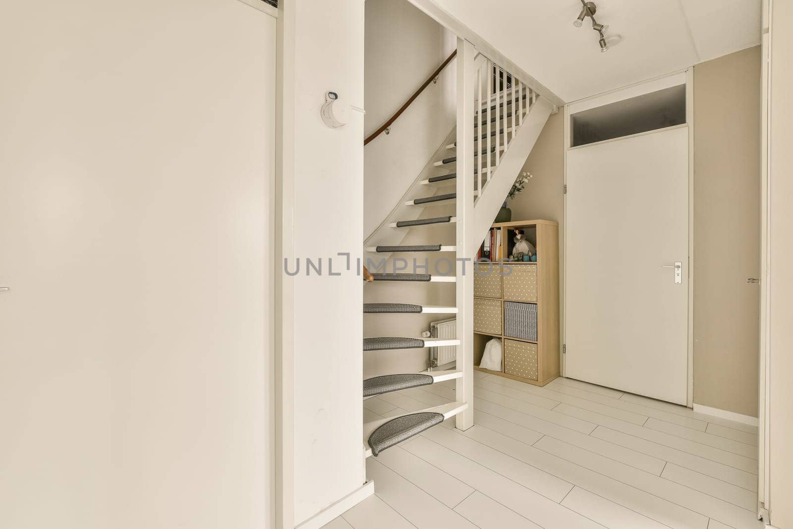 a white room with stairs and shelves on the wall next to an open door that leads to a small hallway