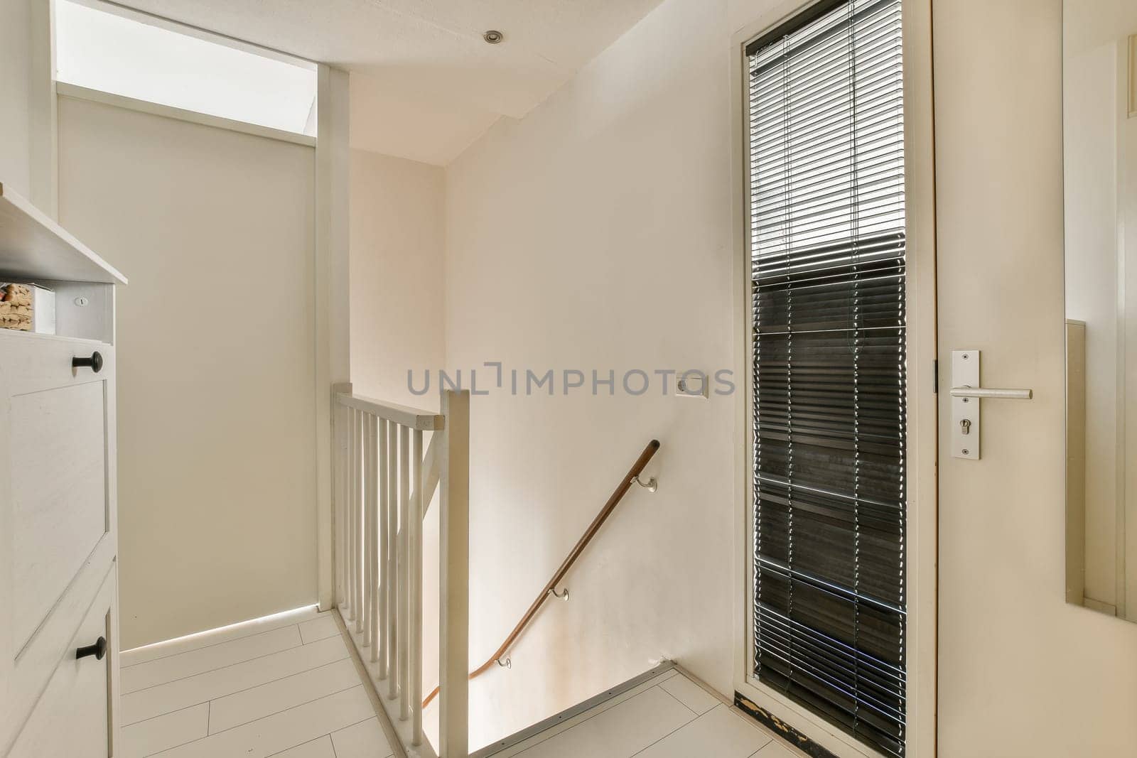 a hallway with white walls and black blinds on the window sies in front of the door to the room