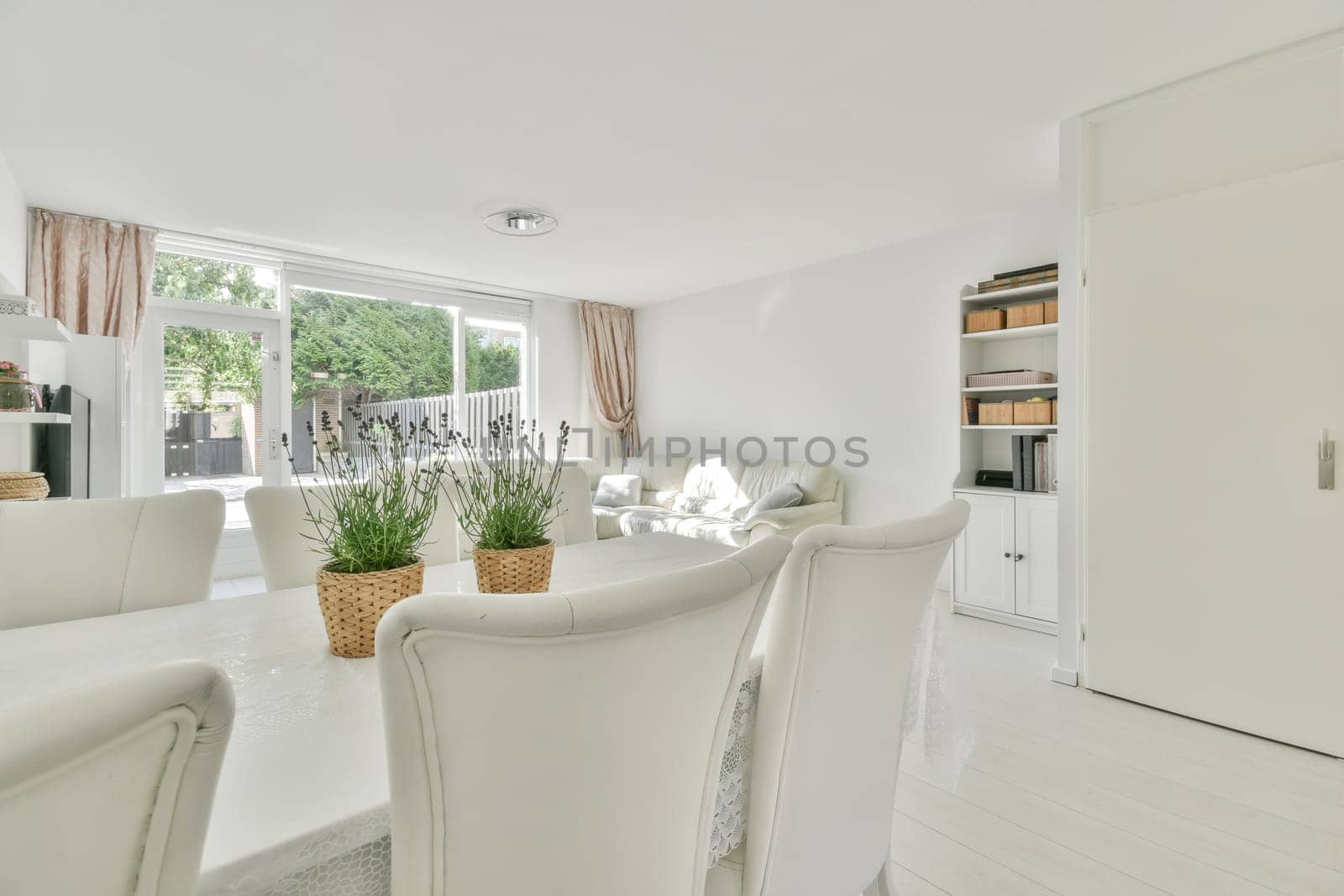 a living room with white furniture and an open door leading to the dining area, which is well lit by natural light