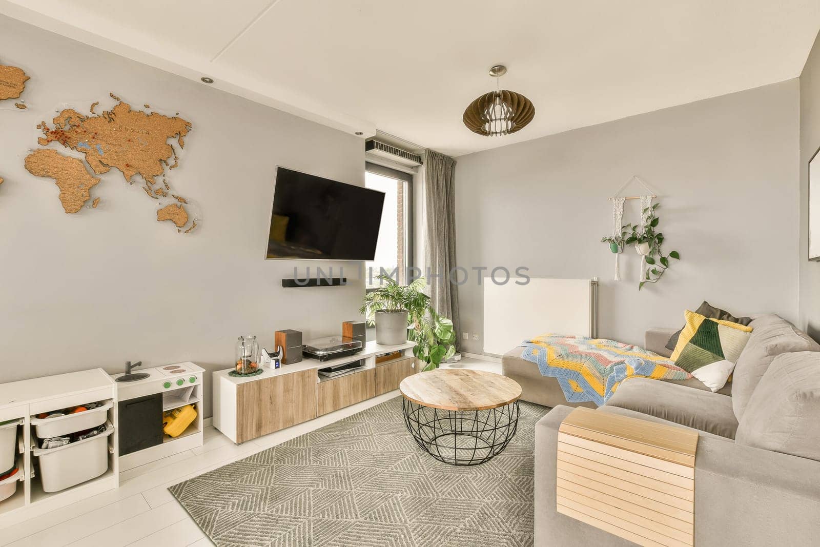 a living room with a map on the wall and a grey couch, coffee table, planters, and tv