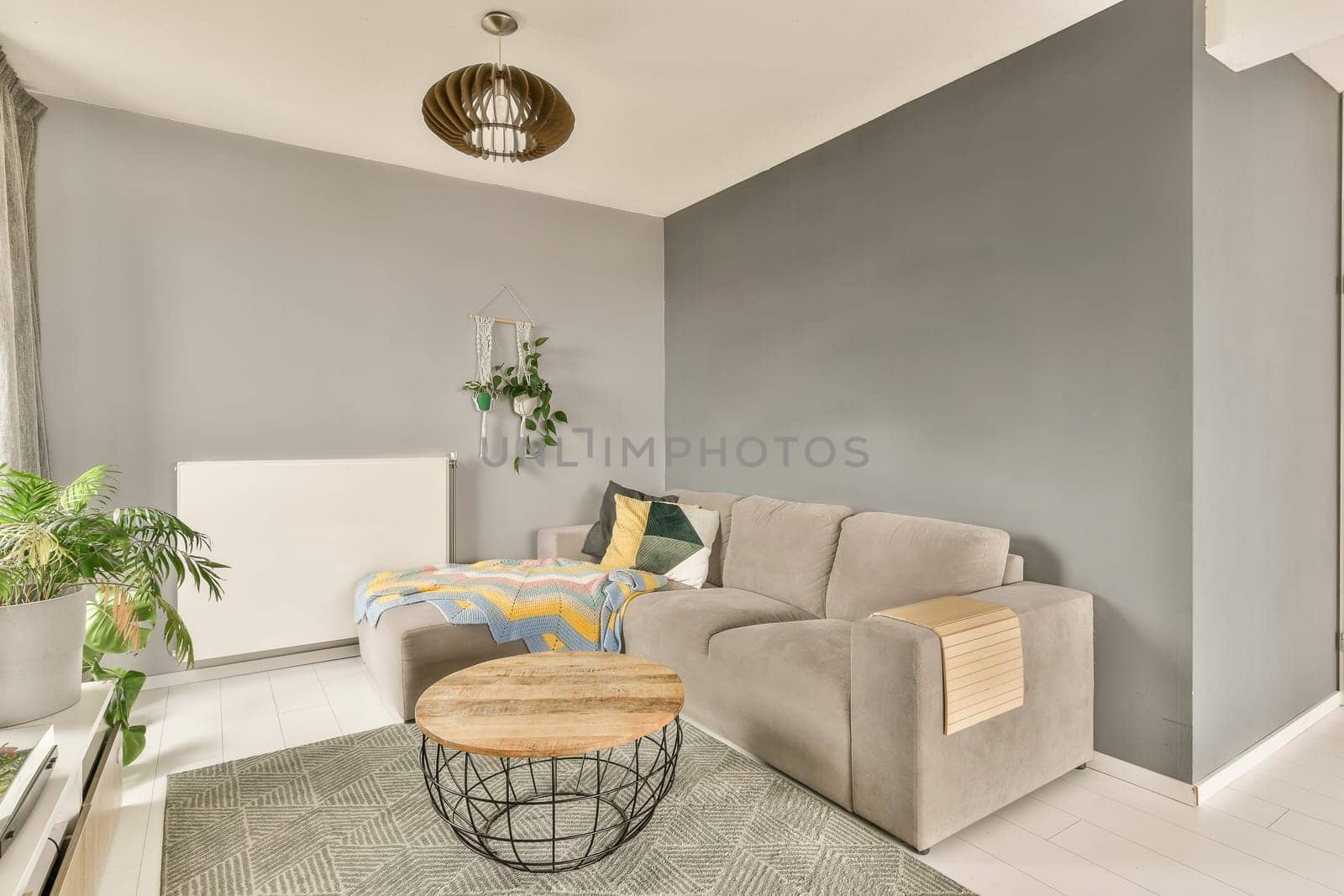 a living room with grey walls and white flooring, including a light gray couch in the corner of the room