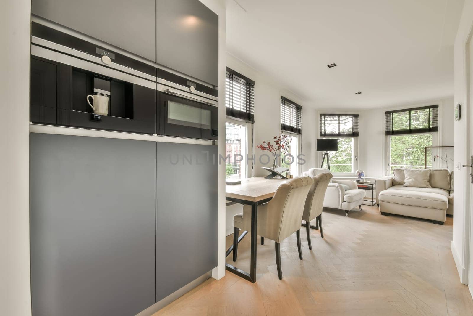 a kitchen and dining area in a modern home with white walls, hardwood flooring and dark grey cabinetry