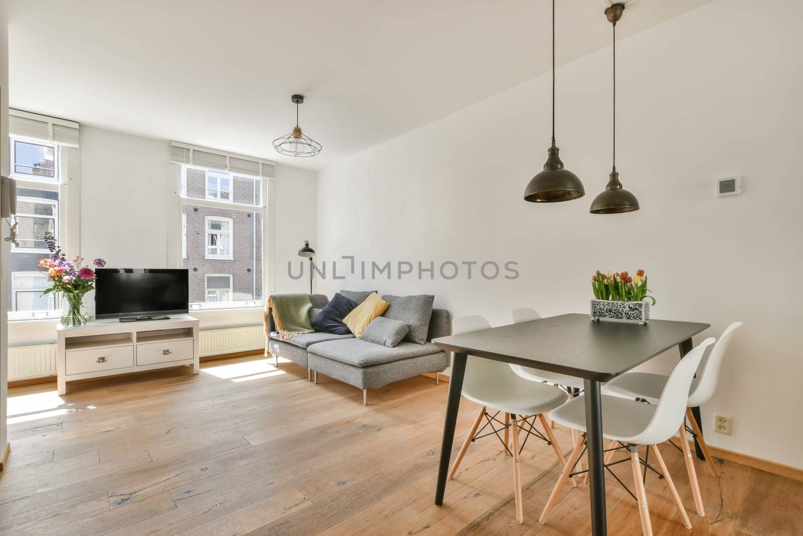 a living room with white walls and hardwood flooring, including a small dining table surrounded by two grey chairs