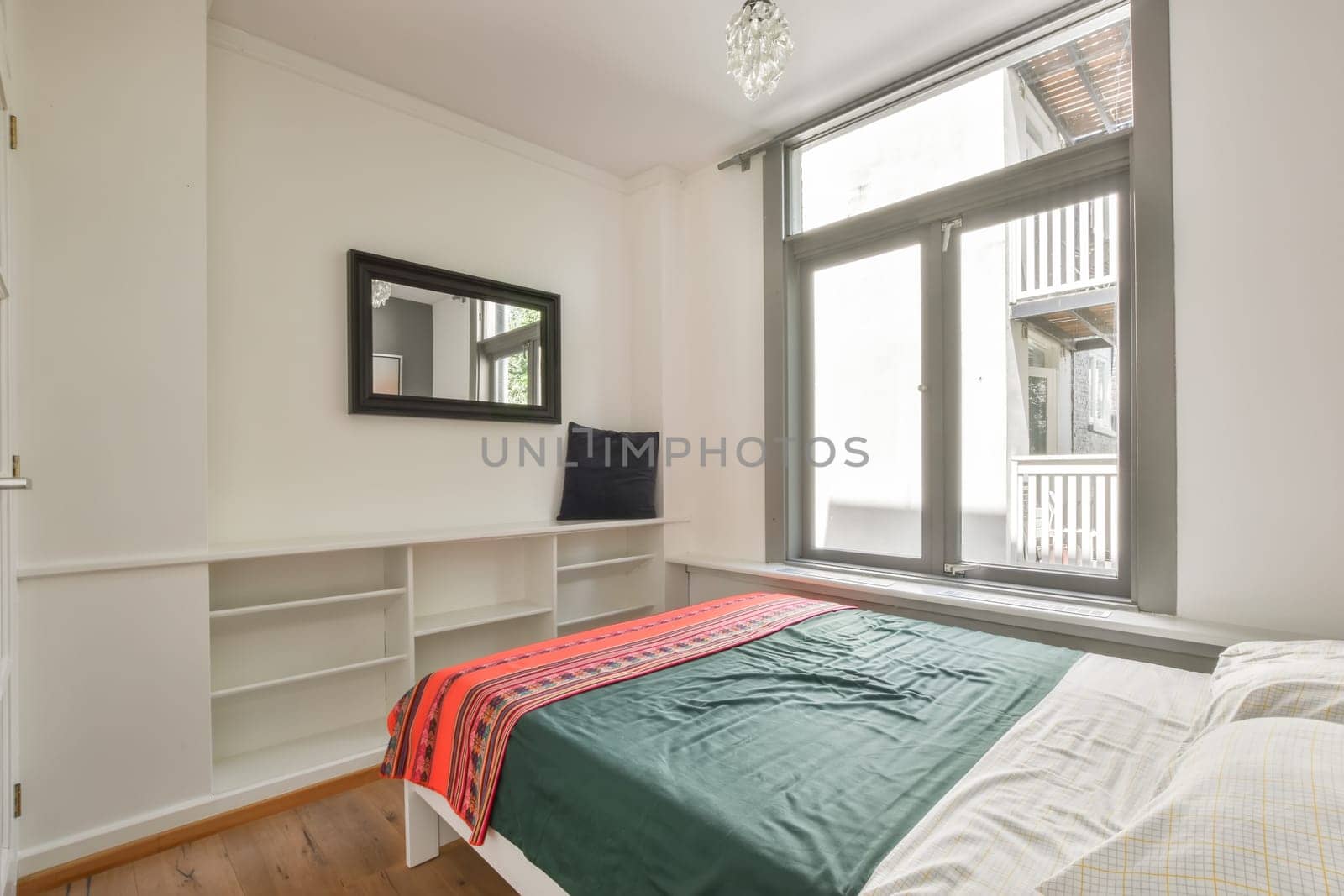 a bedroom with a tv on the wall and a bed in front of a window that has a green blanket