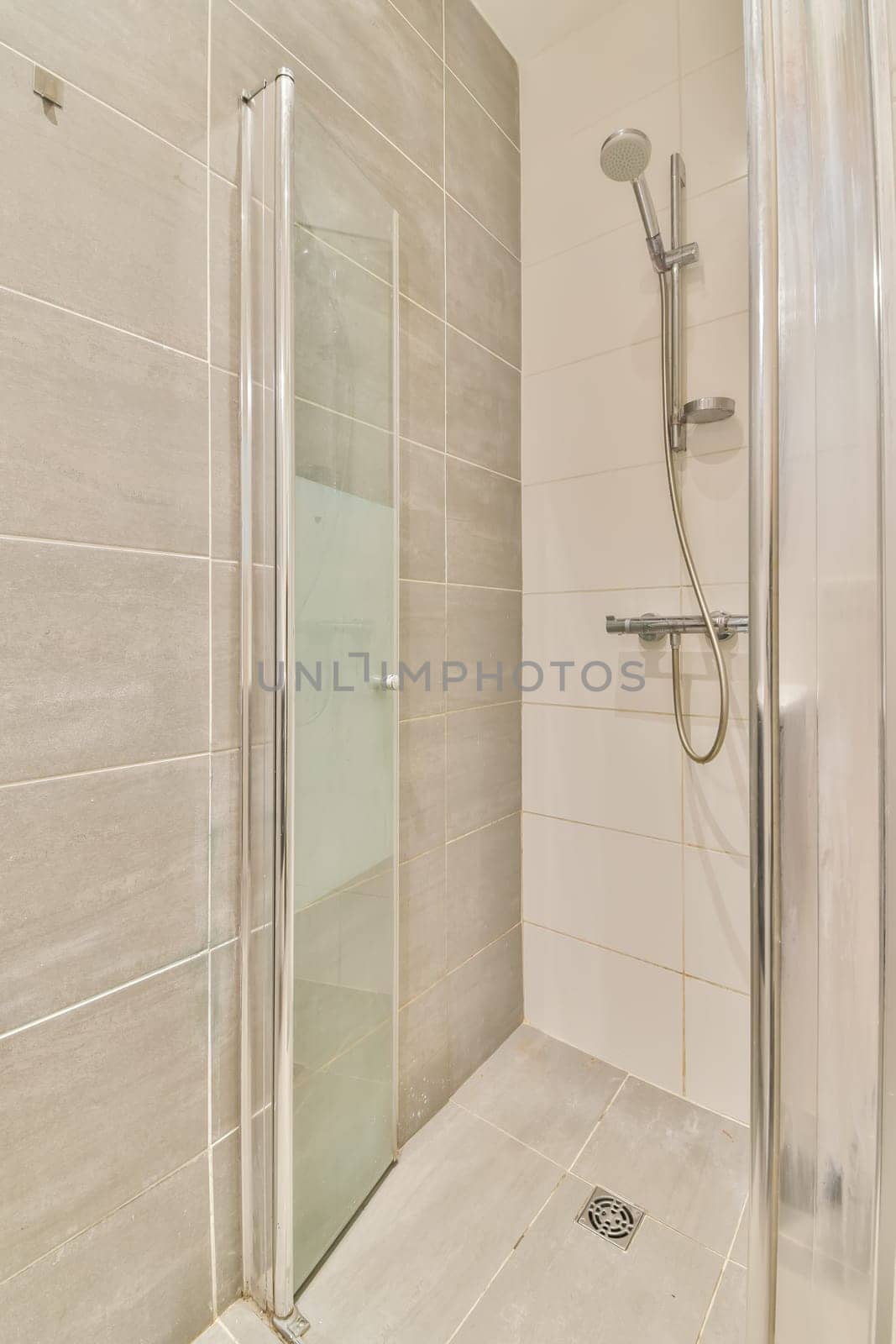 a bathroom with a shower stall and toilet roll on the left hand side, there is a white tiled wall