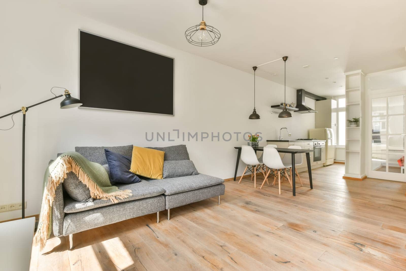a living room with white walls and wood flooring the couch is grey, yellow and green pillows are on the sofa