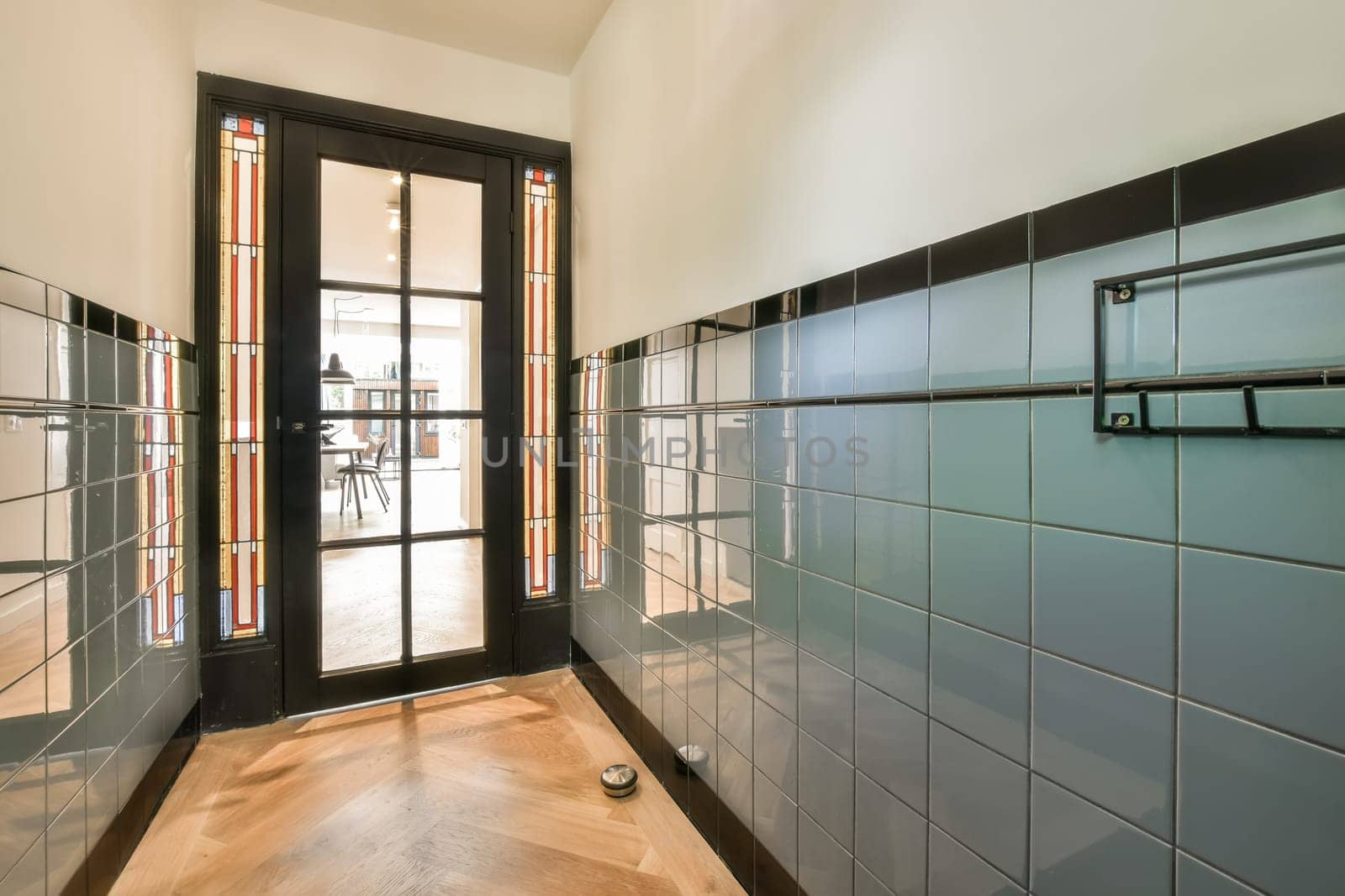 a hallway with glass doors and tiled walls on both sides, leading to an open door that leads into the dining area