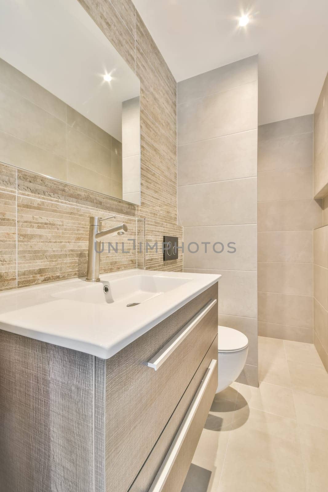 a modern bathroom with beige tile walls and white counters, along the wall is a large mirror above the sink
