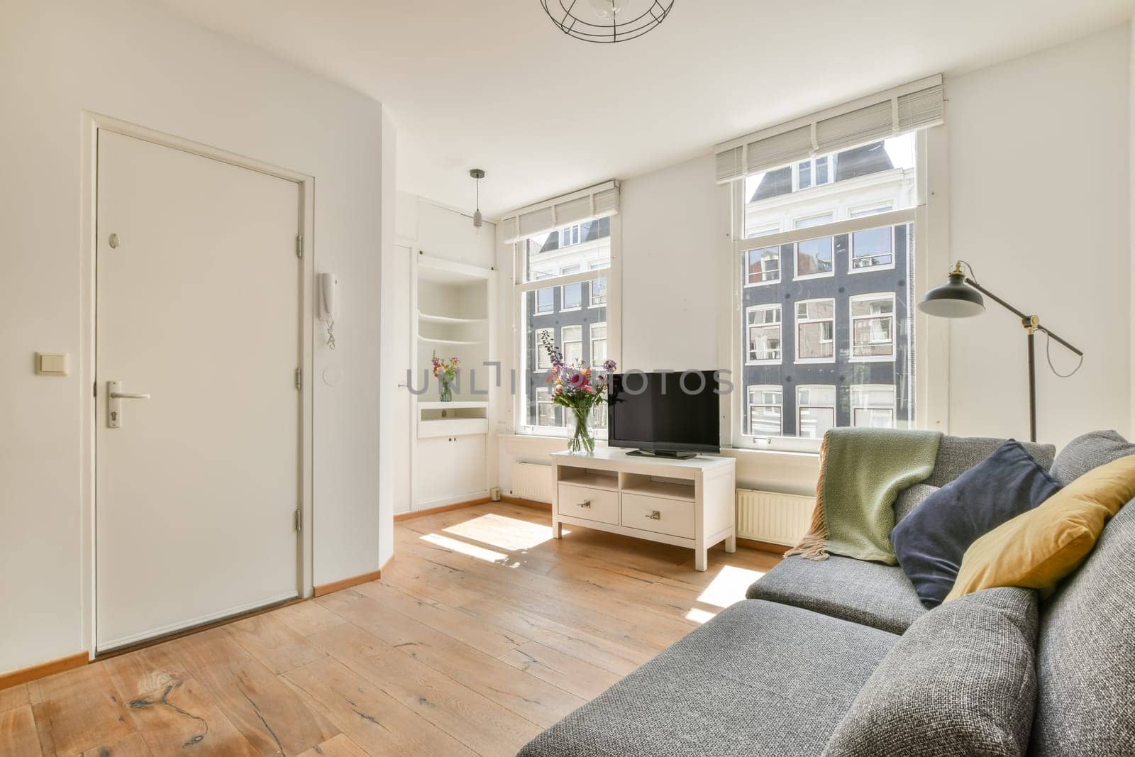 a living room with wood flooring and white walls, including a grey sofa and a tv on the wall
