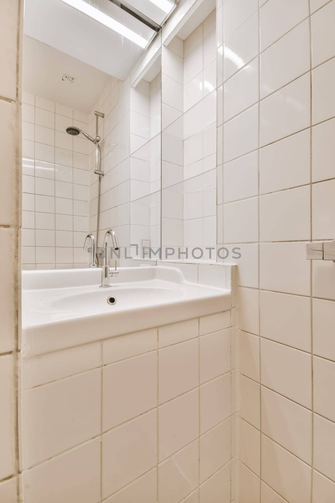 a bathroom with white tiles on the walls, and a mirror in the corner to the sink is next to it