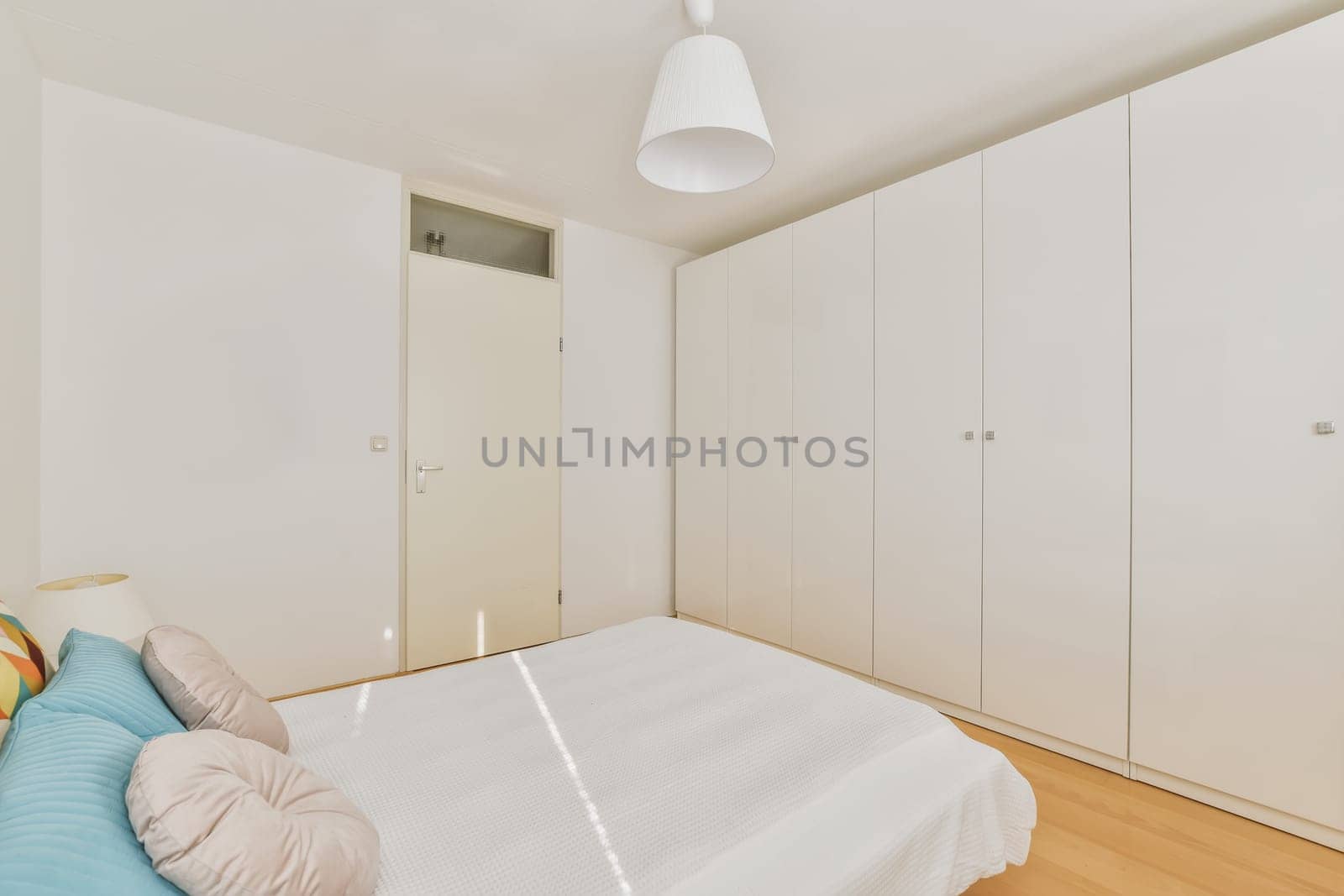 a bedroom with white walls and wood flooring the room has a bed, cabinetd cupboards and wardrobes