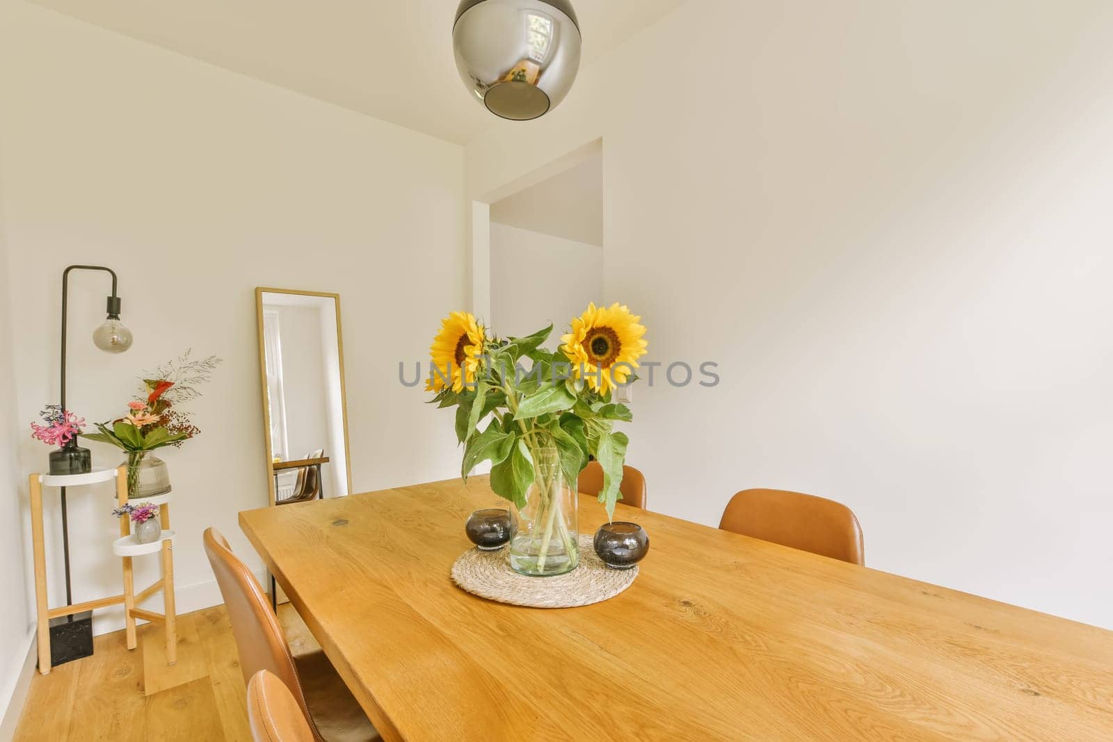 a dining room with sunflowers in a glass vase on the wooden table and two chairs at the wall is white