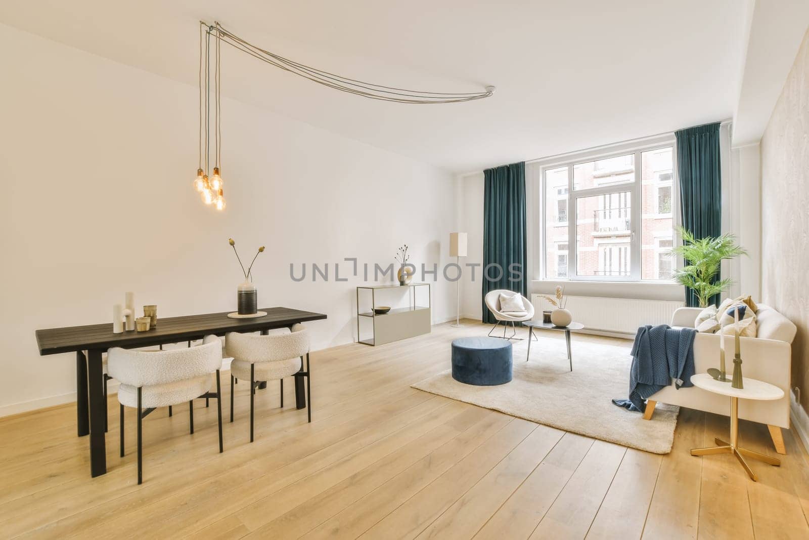 a living room with wood flooring and white walls, including a black dining table surrounded by blue drapes