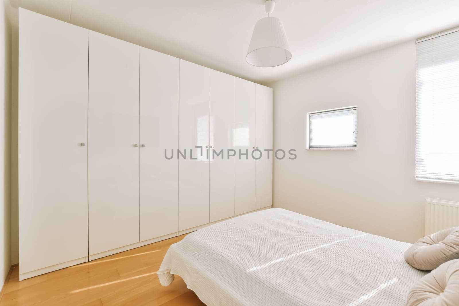 a clean white bedroom with wood flooring and built in wardrobes on the left side of the room, there is a window