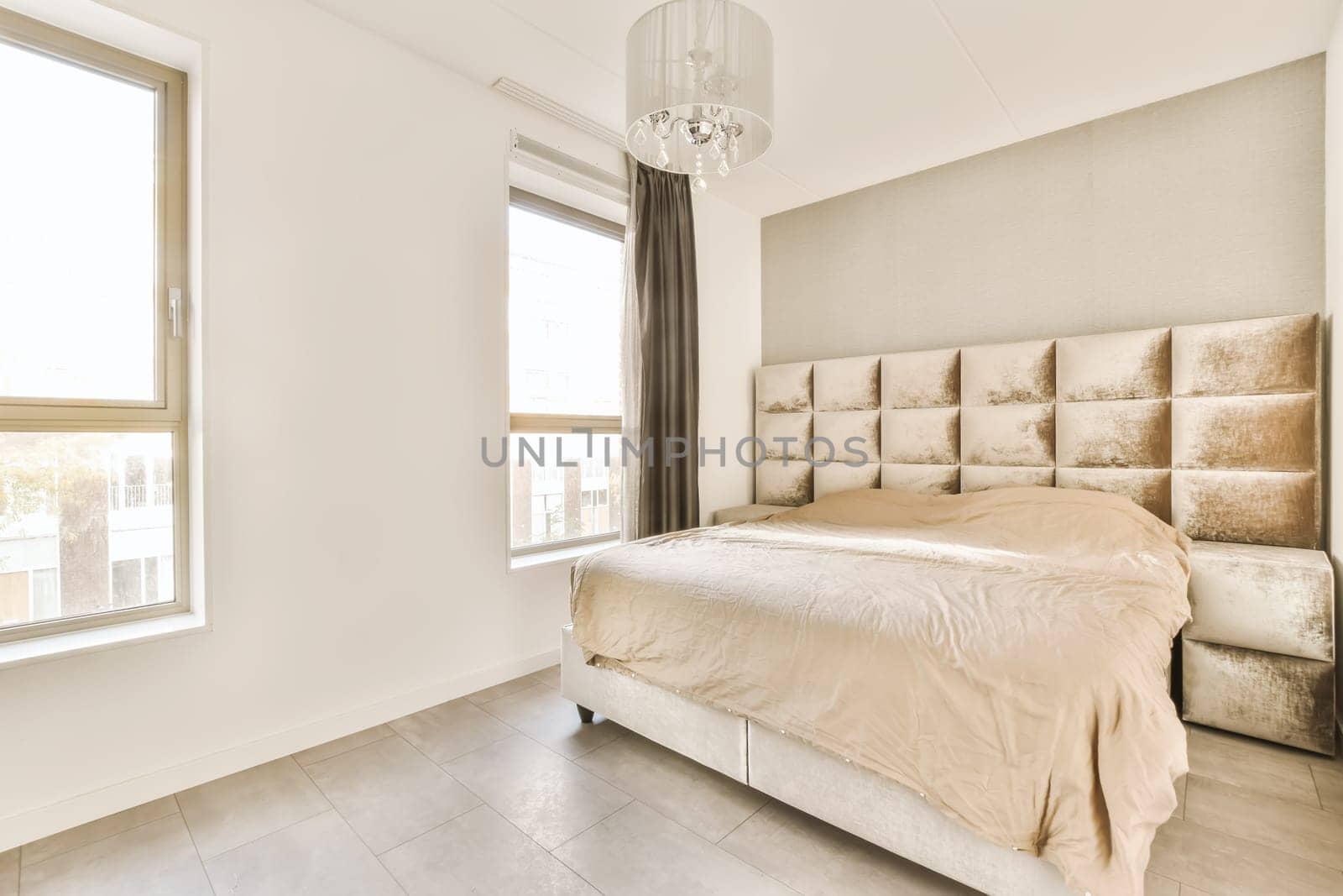 a bedroom with white walls and beige bedding in the middle of the room, there is a chandel on the headboard