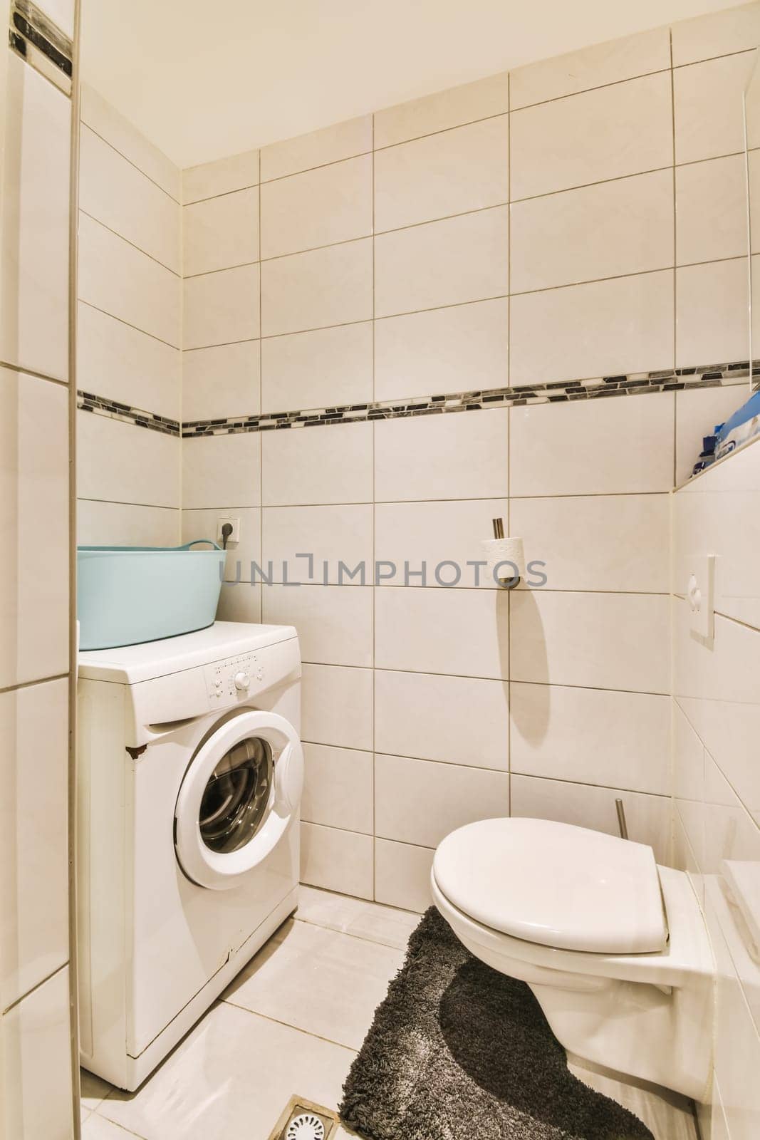 a small bathroom with a toilet and washer in the corner, while it is white tile on the walls