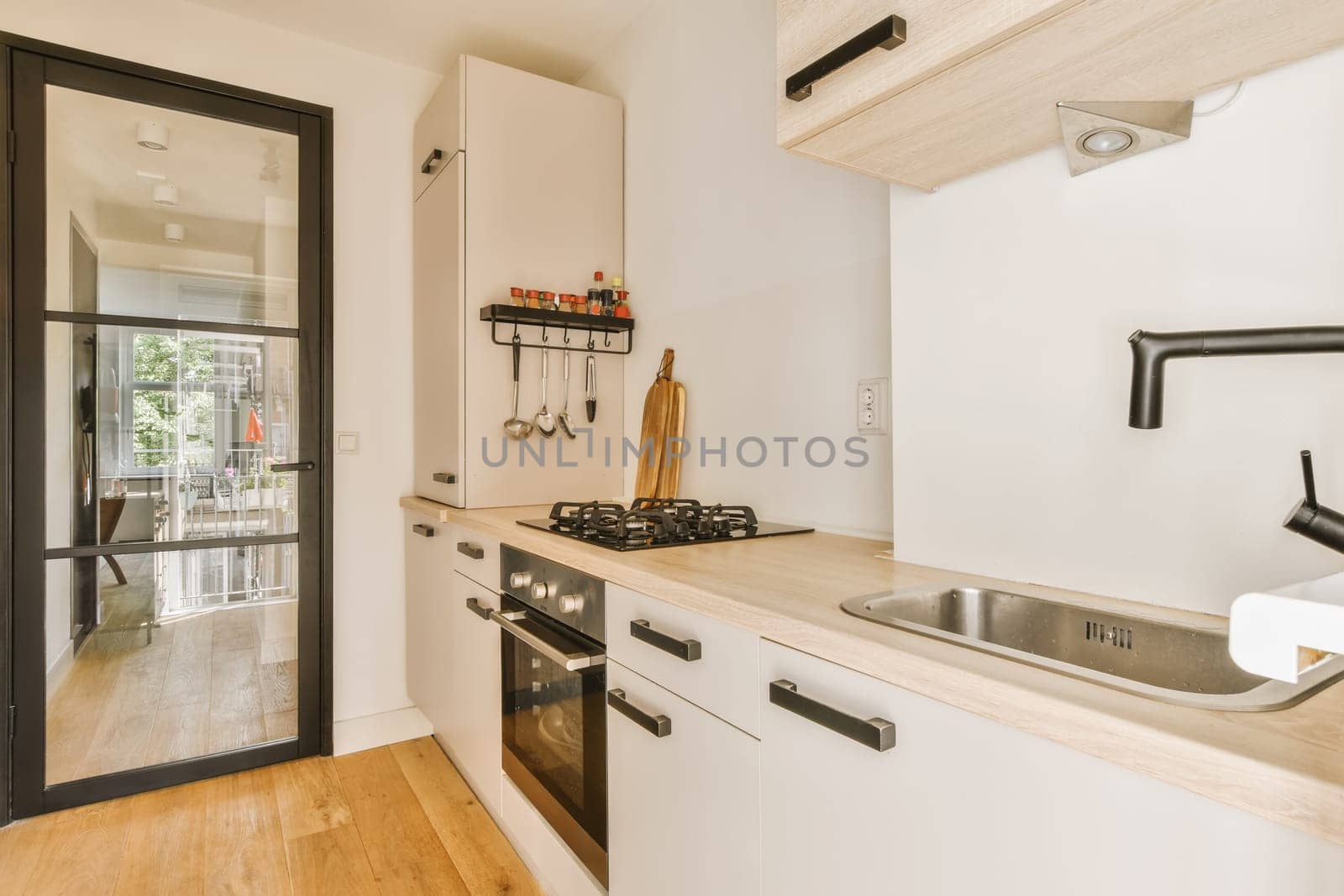 a kitchen with wood flooring and white cupboards, black door handles, and an oven in the corner