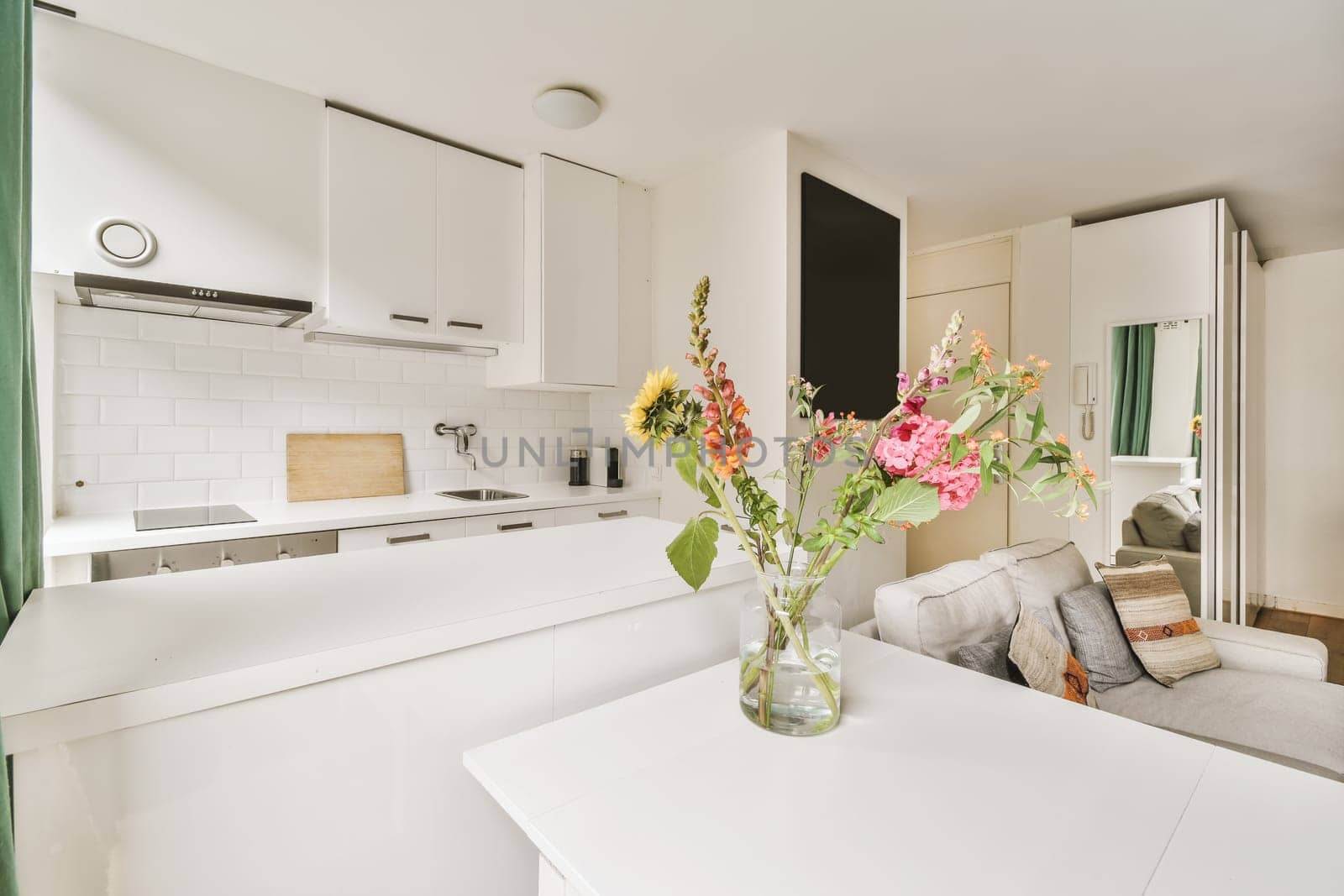 some flowers in a vase on a kitchen table with white cupboards and green drapes behind the counter area