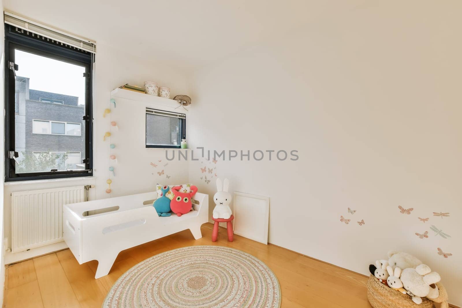 a kid's room with white walls and wooden flooring, including a large round rug on the floor