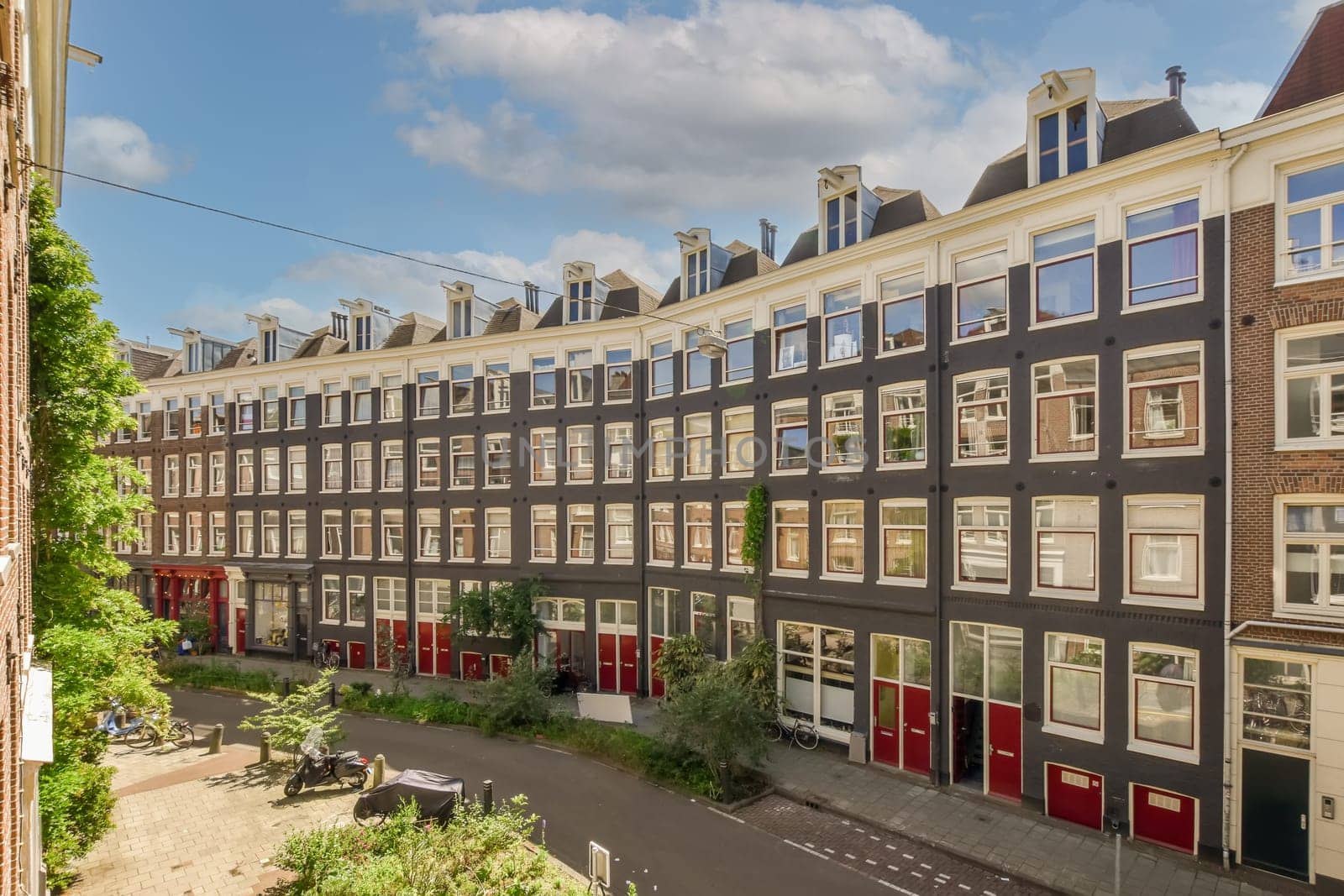 a street in the city with many houses and buildings on either side, one building has red shuttered windows