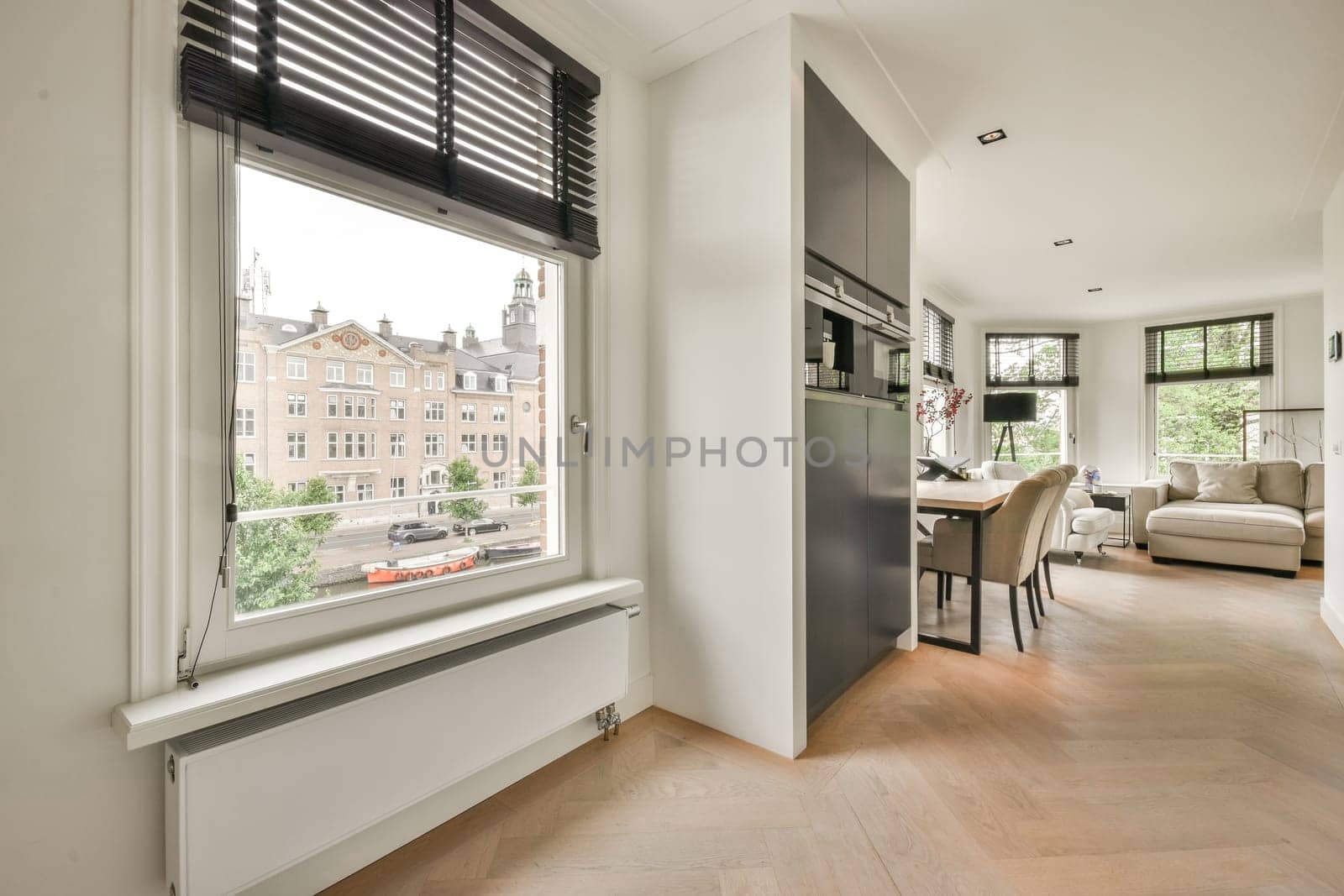 a living room with wood flooring and white walls there is a dining table in front of the large window