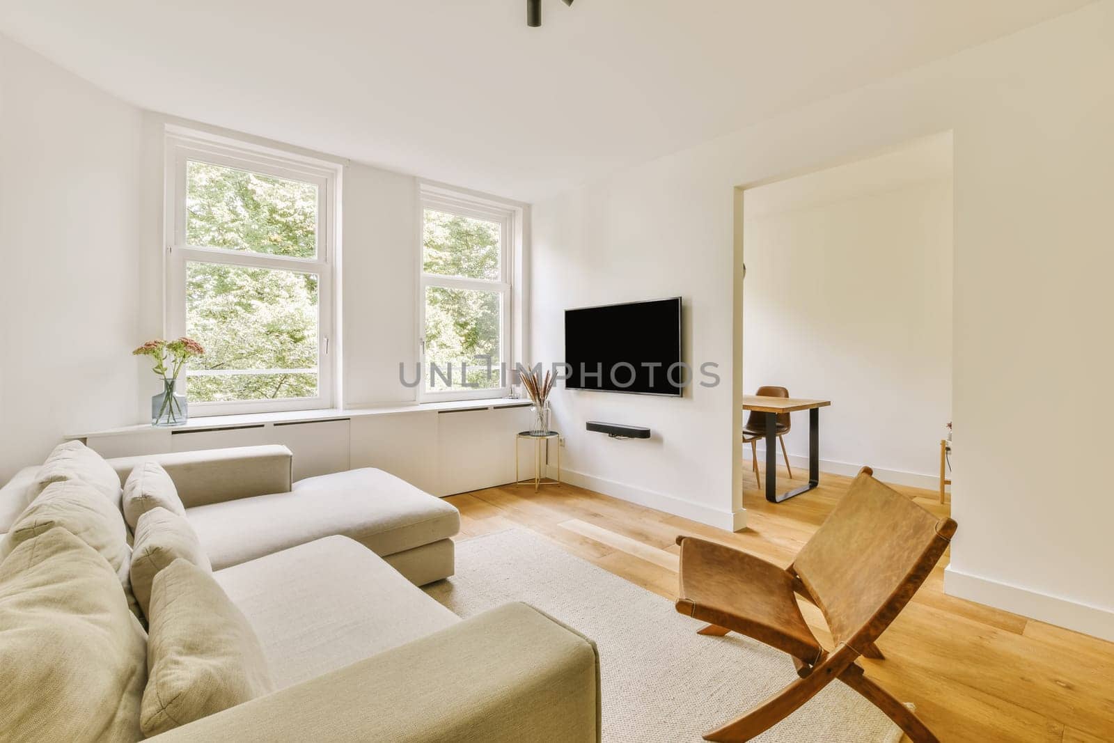a living room with white walls and hardwood flooring, there is a flat screen tv mounted on the wall