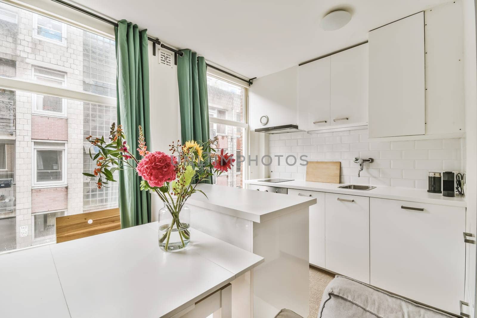 a white kitchen with flowers in the vase on the counter and window to the left, looking out onto the street