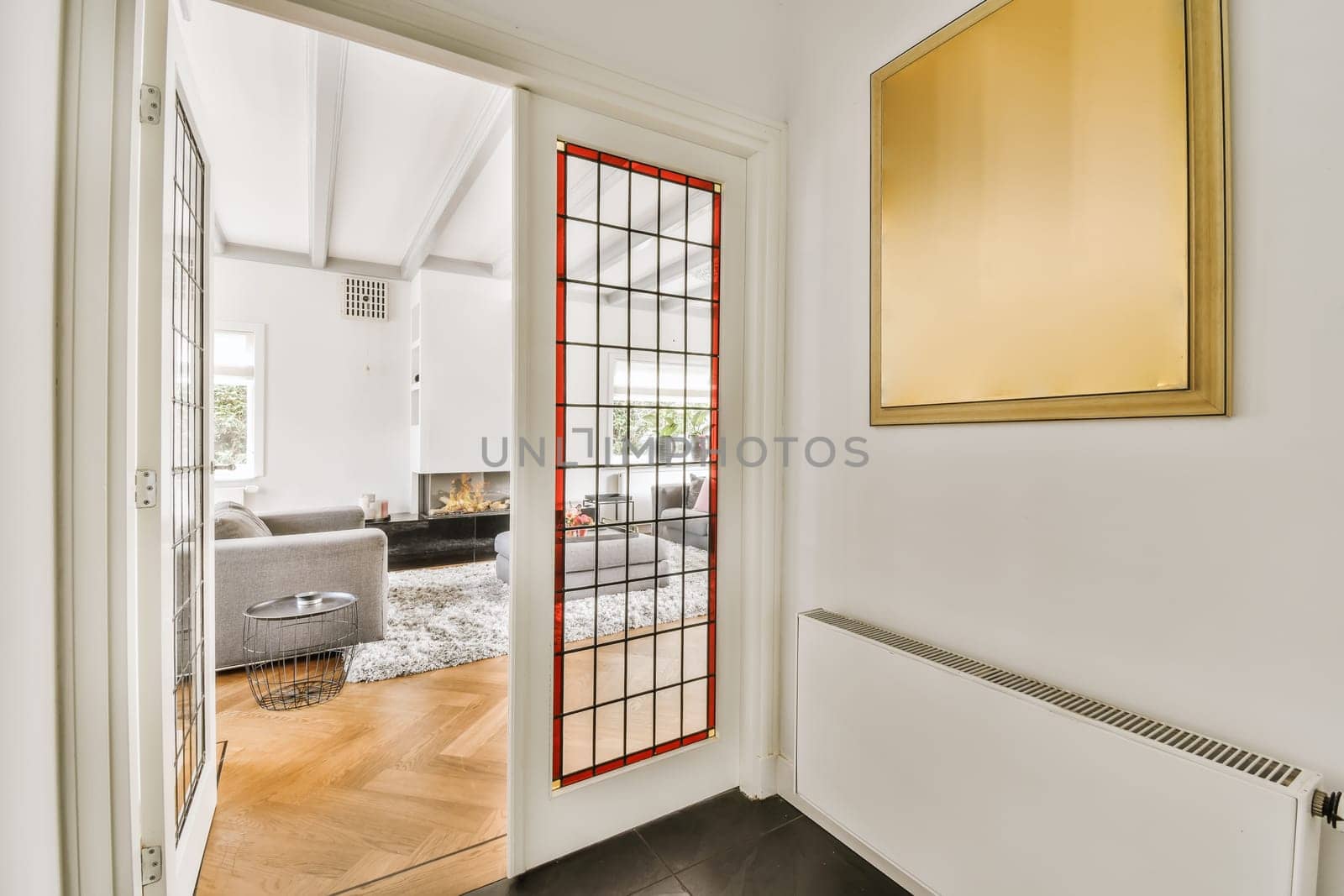 a living room with white walls and wood flooring, framed by a red glass paneled door that leads to the entryway