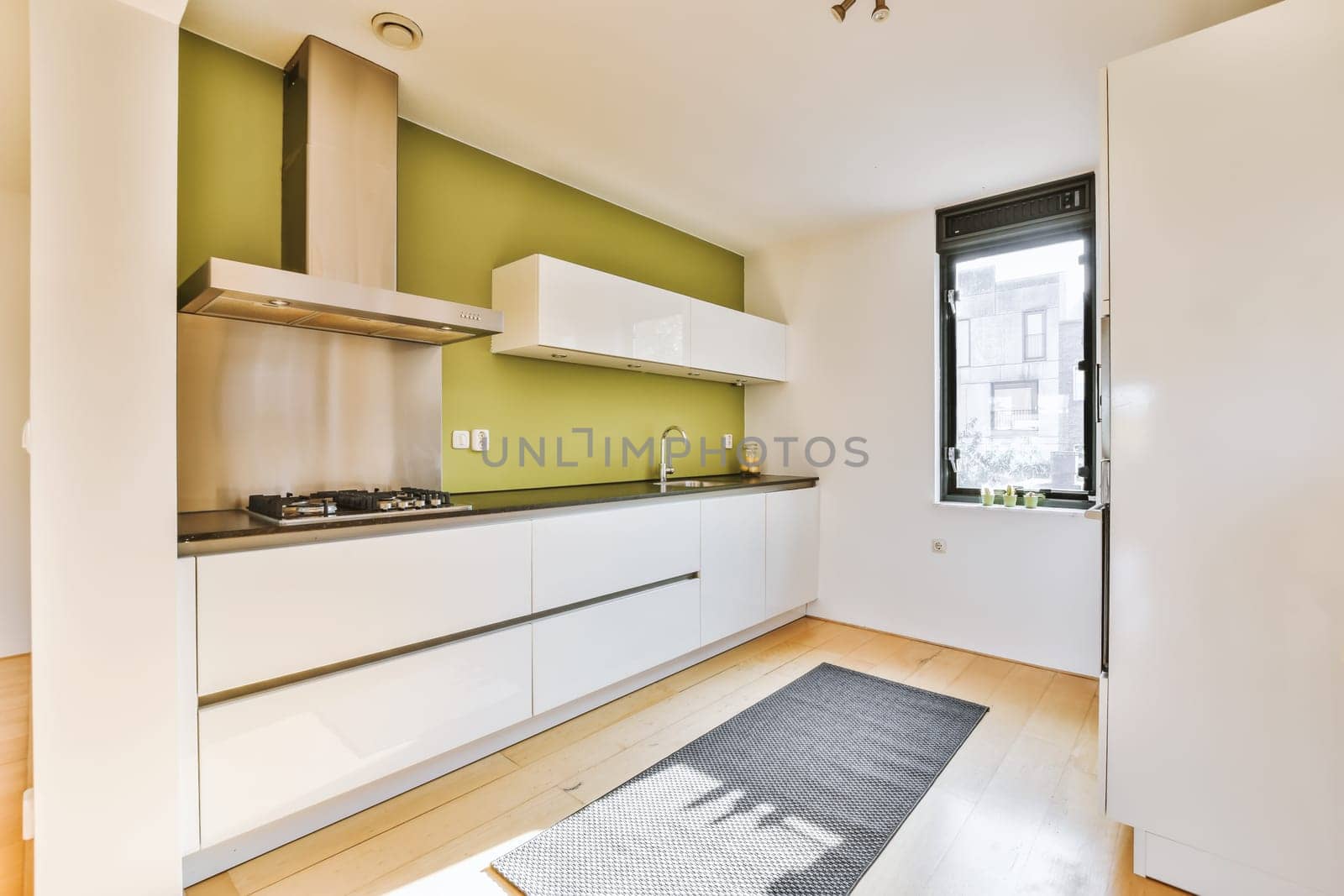 a kitchen area with white cabinets and green accent wall behind the countertop, door to the left is an open window