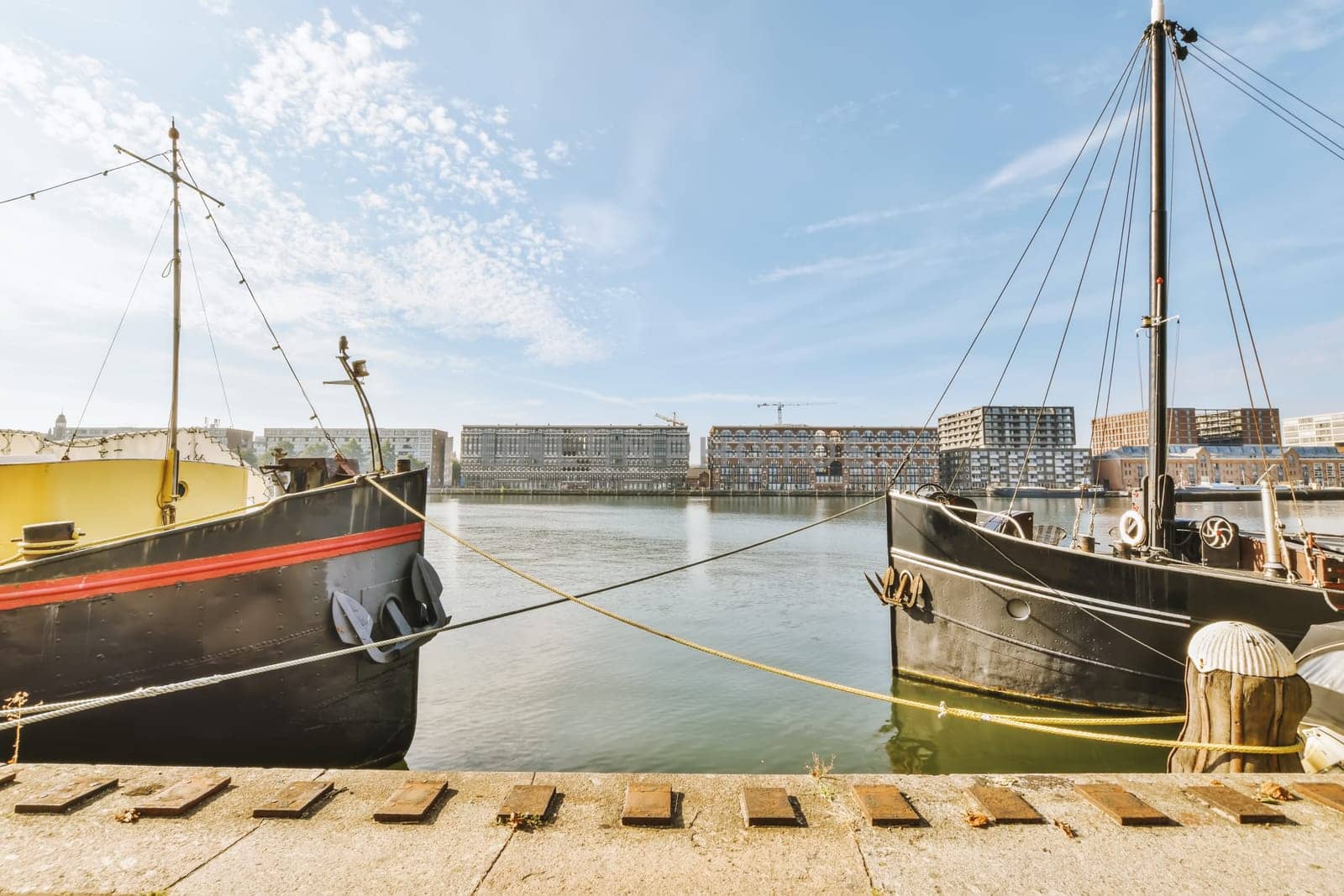 two boats docked at the dock in front of a large building and blue sky with some white clouds above them